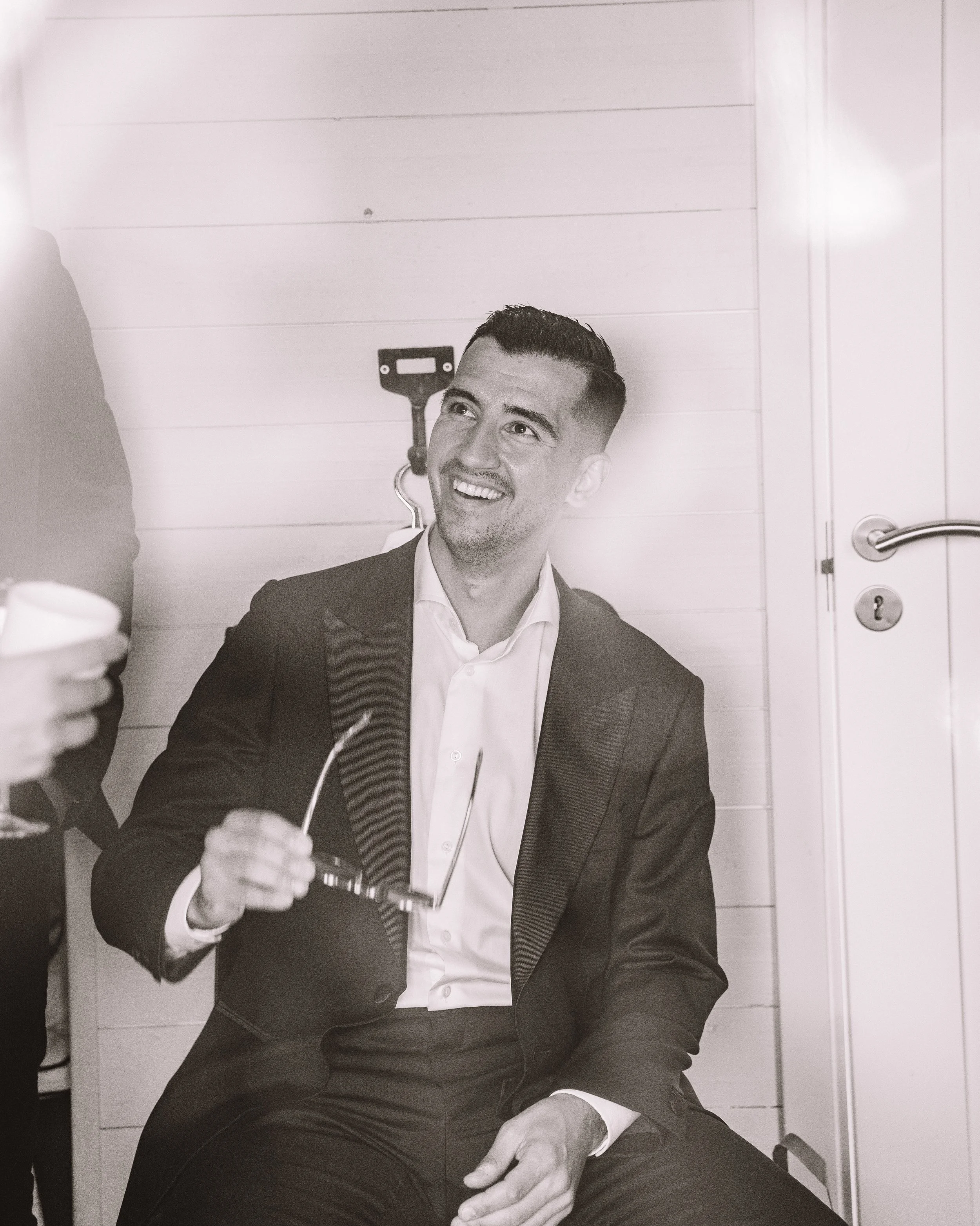 En brudgum i kostym som är sittande i ett rum och ler.