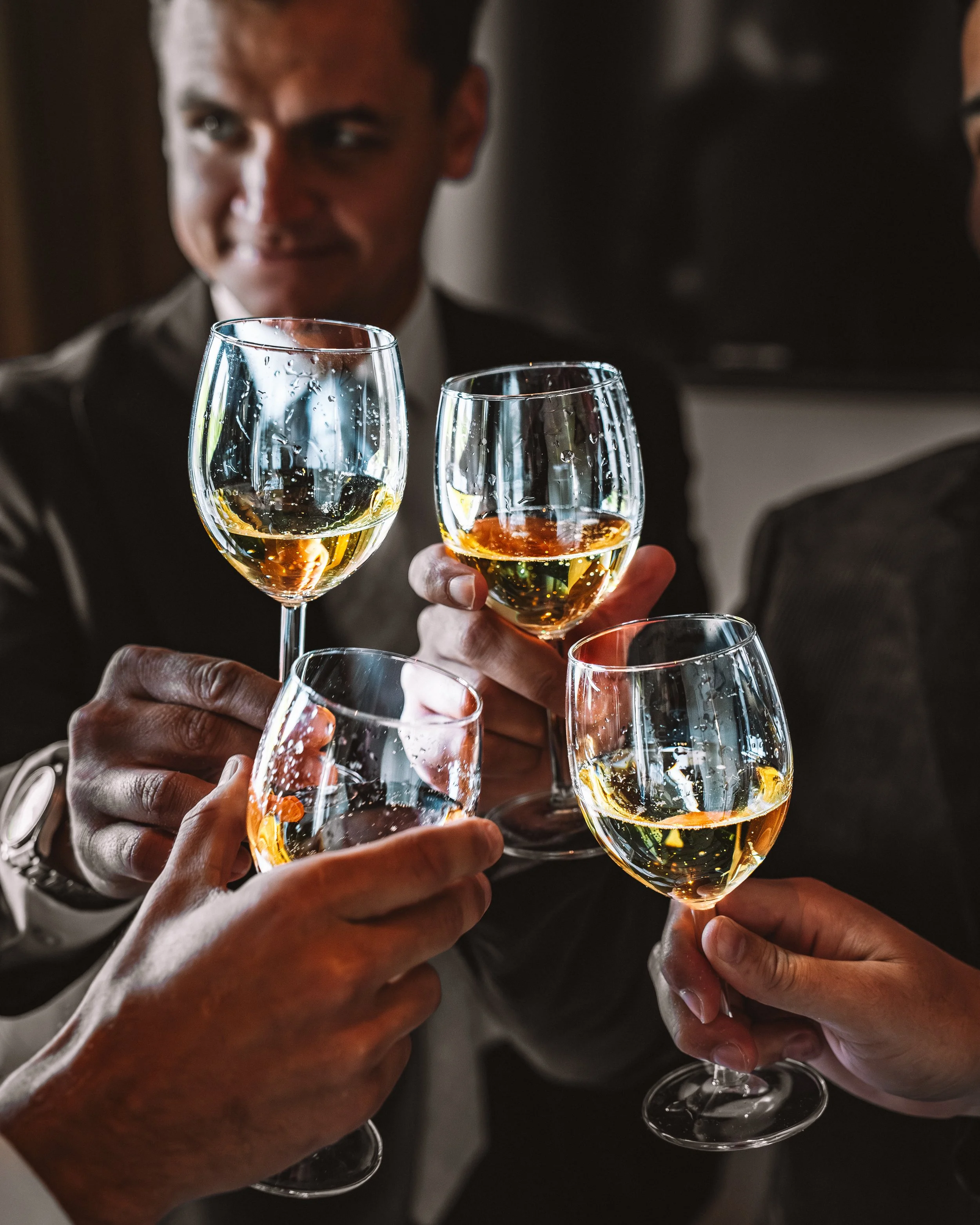 Flera personer som skålar med vita vin i glas, sammanstrålande i en trevlig samling.