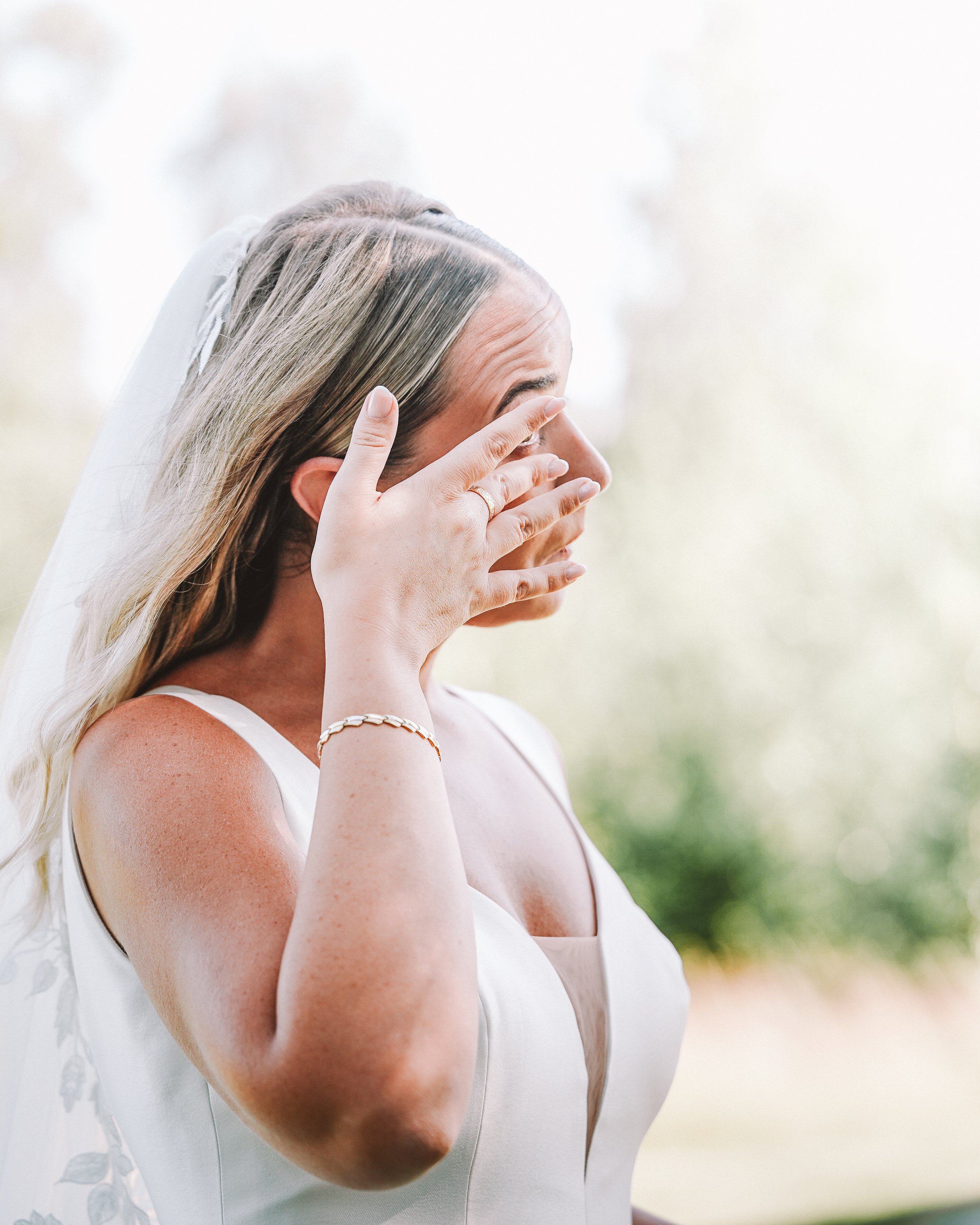Brud kvinna i brudklänning med hand vid ansiktet, promenerar utomhus.