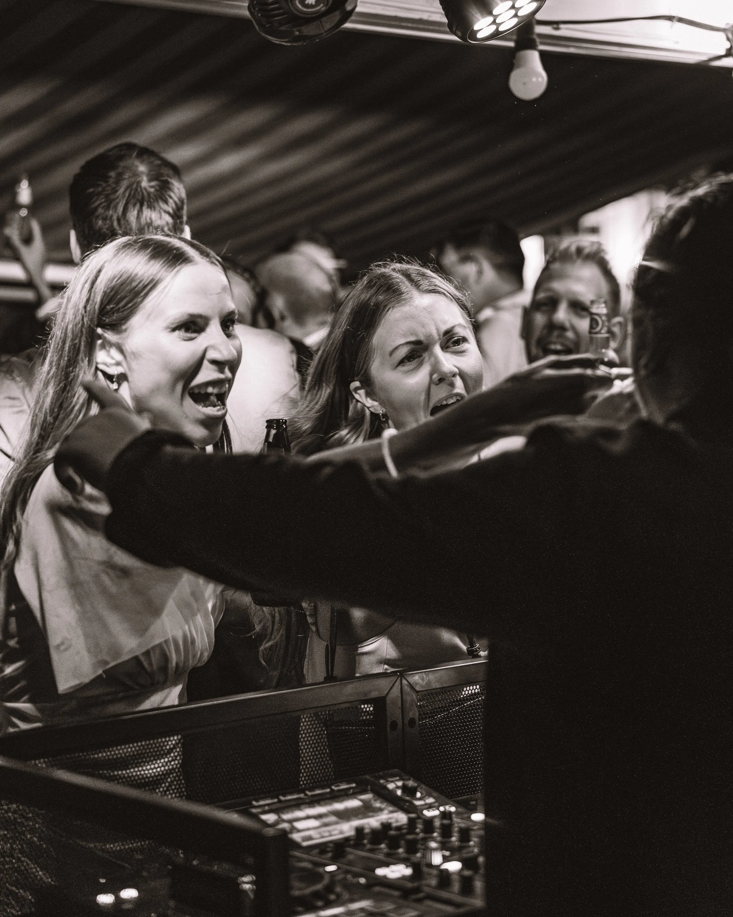 Svartvitt foto av en klubb eller fest med människor. Tre personer i förgrunden, två kvinnor och en man, visar starka uttryck i ansiktena.