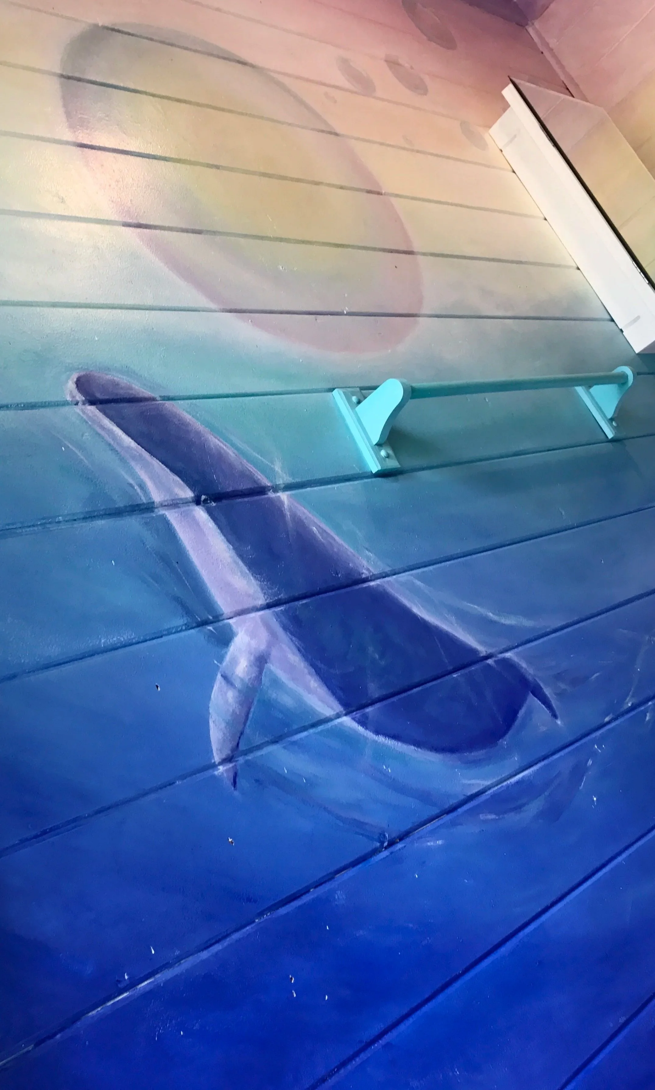 A rainbow mural on a wooden wall depicting a whale jumping out of water with bubble floating above.