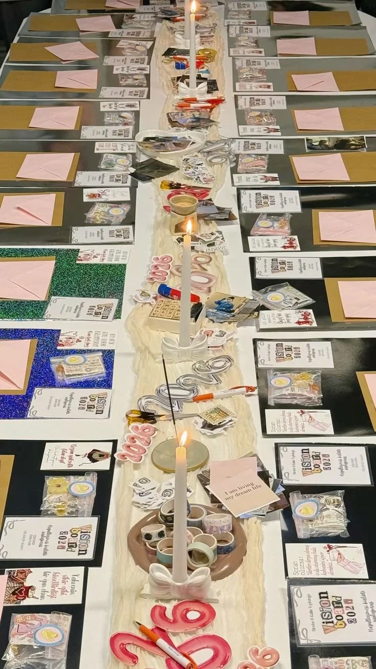 Decorated long table with candles, pink and black accents, and name cards, set for a creative workshop event, with a washi tape, collage supplies, and taper candles as table settings.