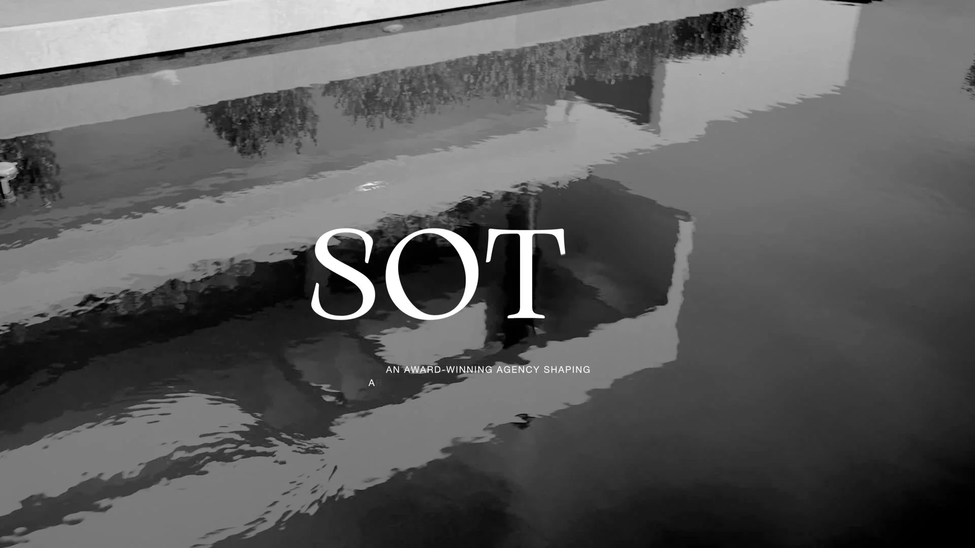 Black and white photograph of a building reflected in a body of water with the words "SOT" and smaller text about an award-winning agency shaping
