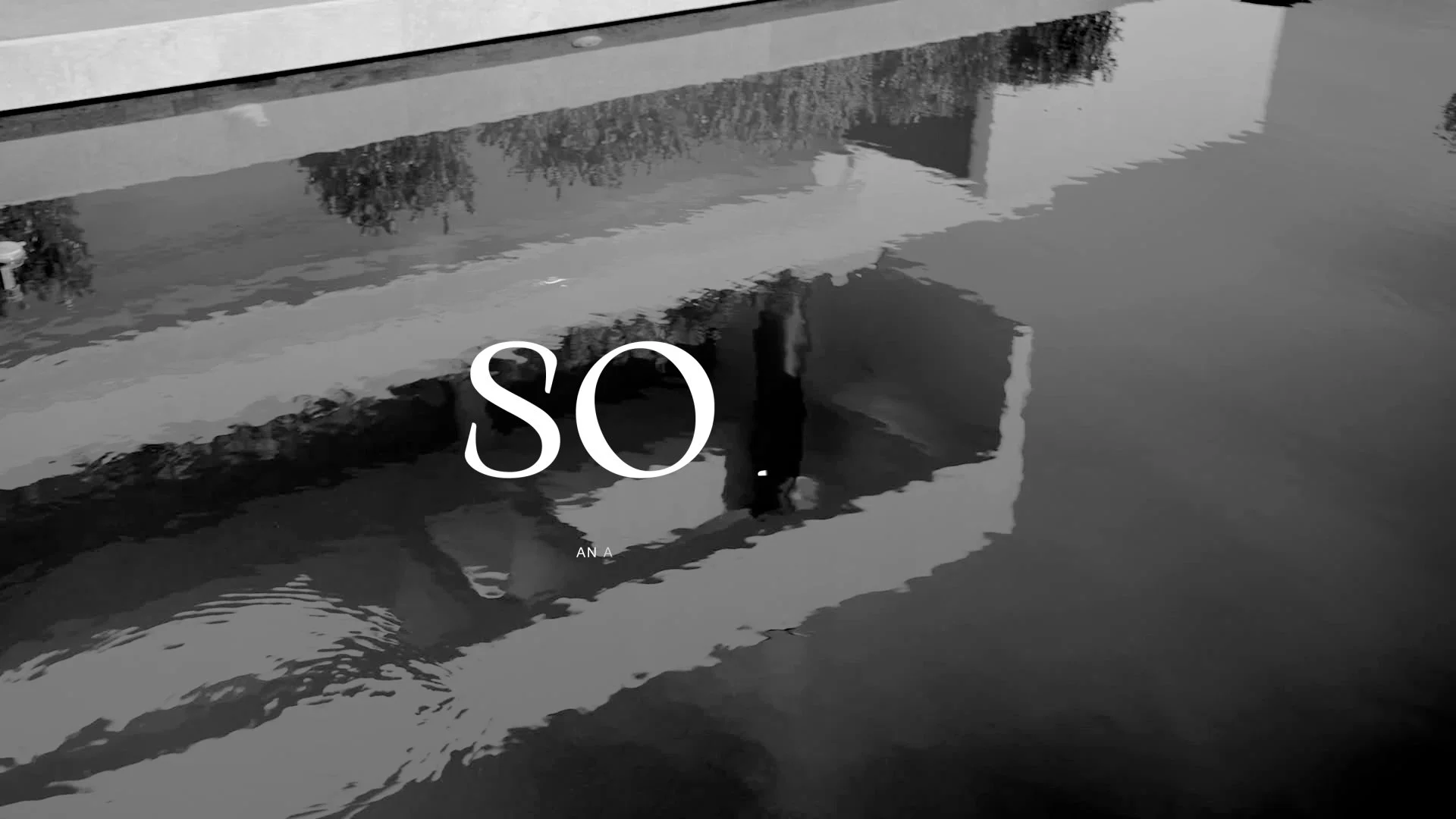 Reflection of a building and trees on water with the partial text 'SO' in overlay.