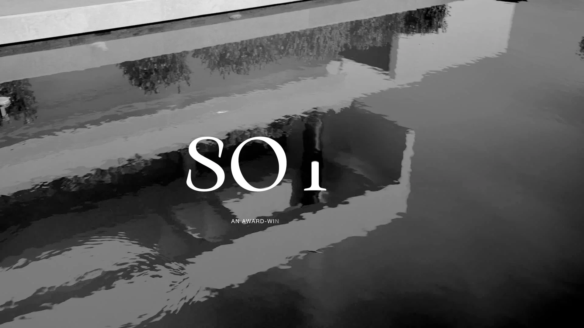 Black and white photo of a swimming pool reflecting the sky, with a building, trees, and a person in the reflection, and overlaid text that reads 'SO 1' and 'AN AWARD-WIN'.
