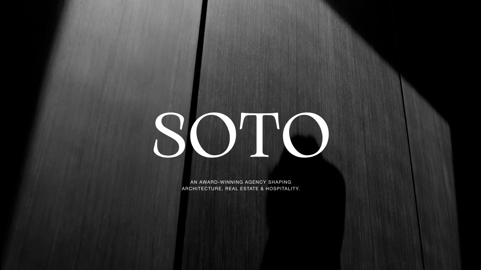 Black and white photo of a wooden wall with shadows, with the large white text "SOTO" and smaller text underneath that reads "An award-winning agency shaping architecture, real estate & hospitality."