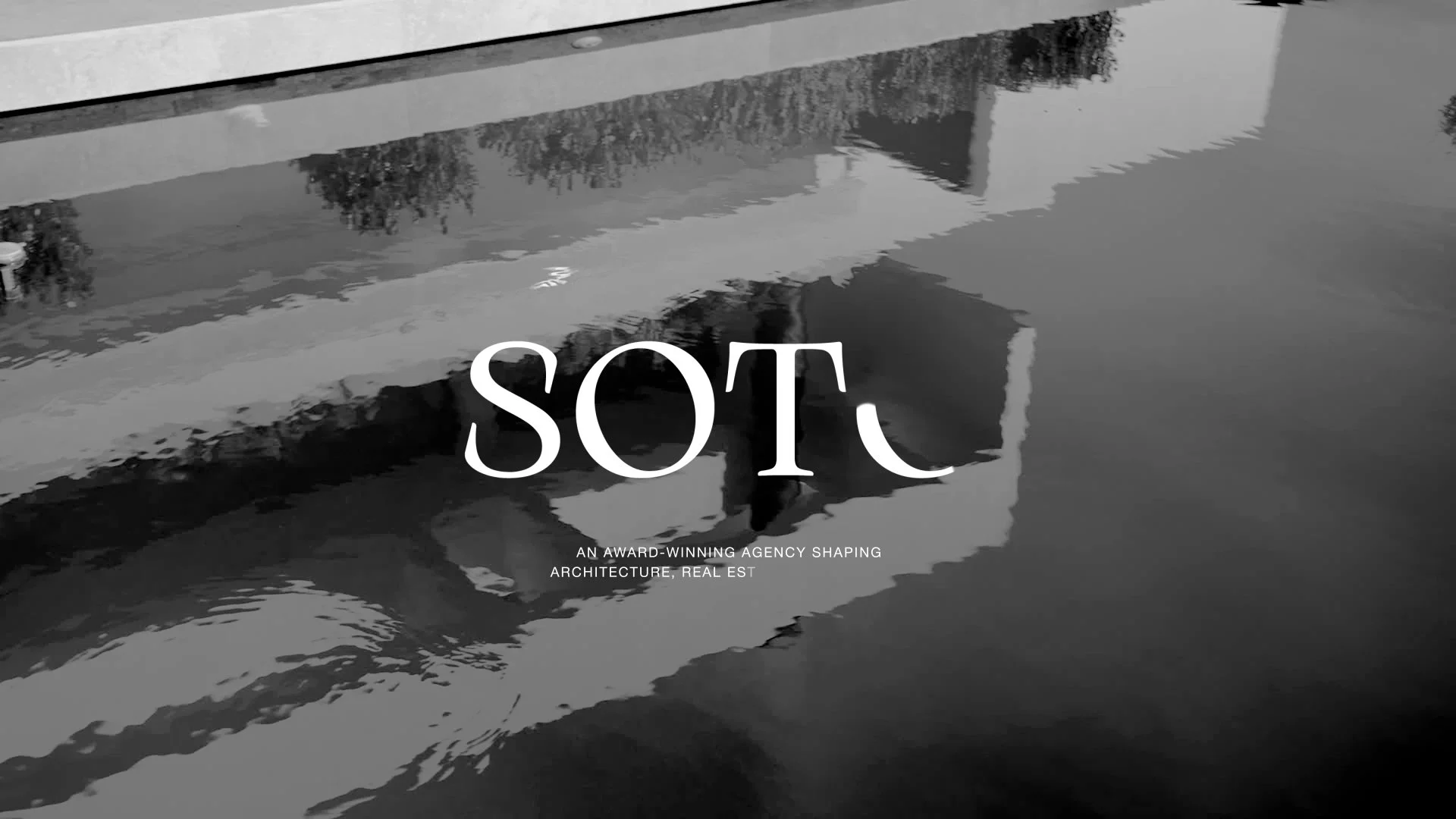 Black and white photograph of a building reflected in a body of water with the word "SOTC" in large font and the text "An award-winning agency shaping architecture, real estate" underneath.