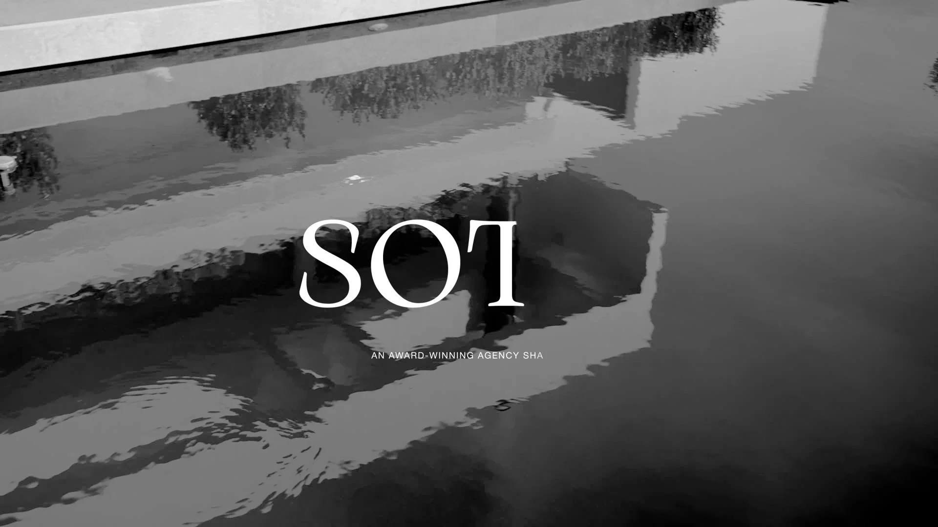 Black and white image of a reflection in water showing a building, trees, and stairs, with the text 'SOL' and the subtitle 'An award-winning agency SHA' overlaid.