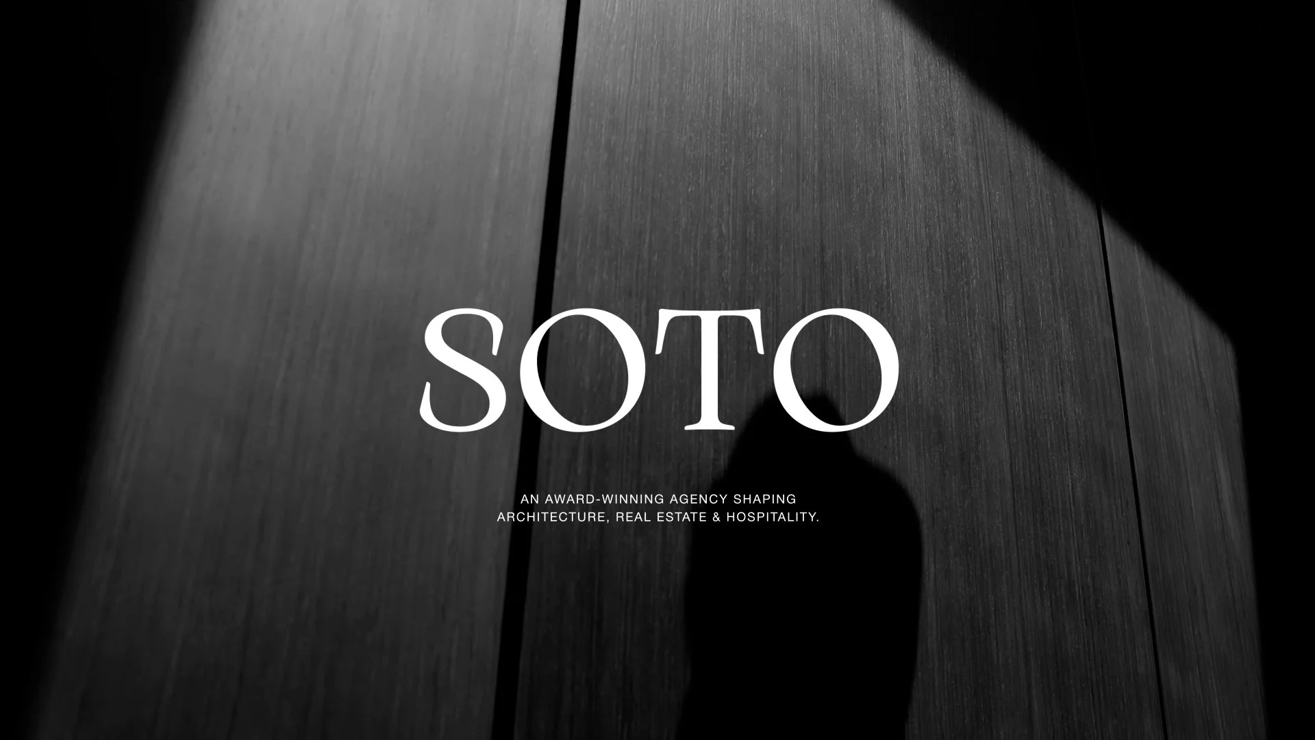 Black and white photo of a wooden wall with shadow and the text 'SOTO' in large white letters, and smaller text below mentioning architecture, real estate, and hospitality.