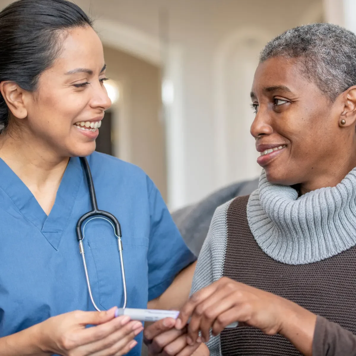 Enfermera sonriendo y entregando un medicamento a una paciente en un entorno clínico.