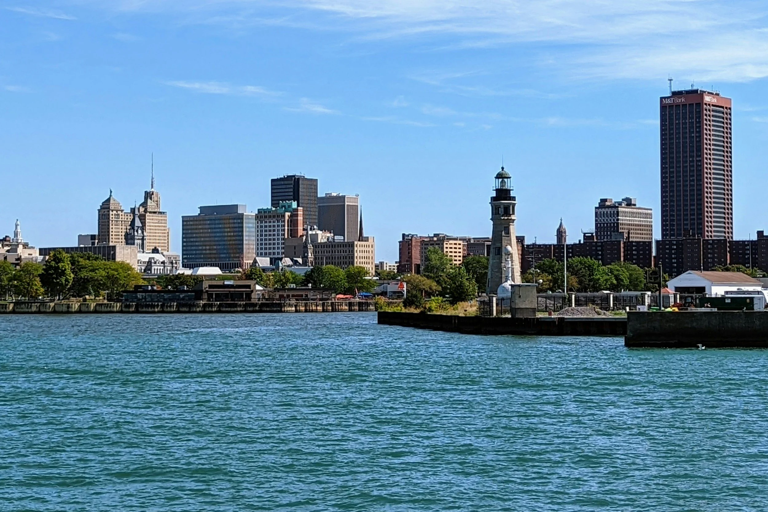 A city skyline viewed across a body of water on a clear day, with various tall buildings including a Red and white M&T Bank building.