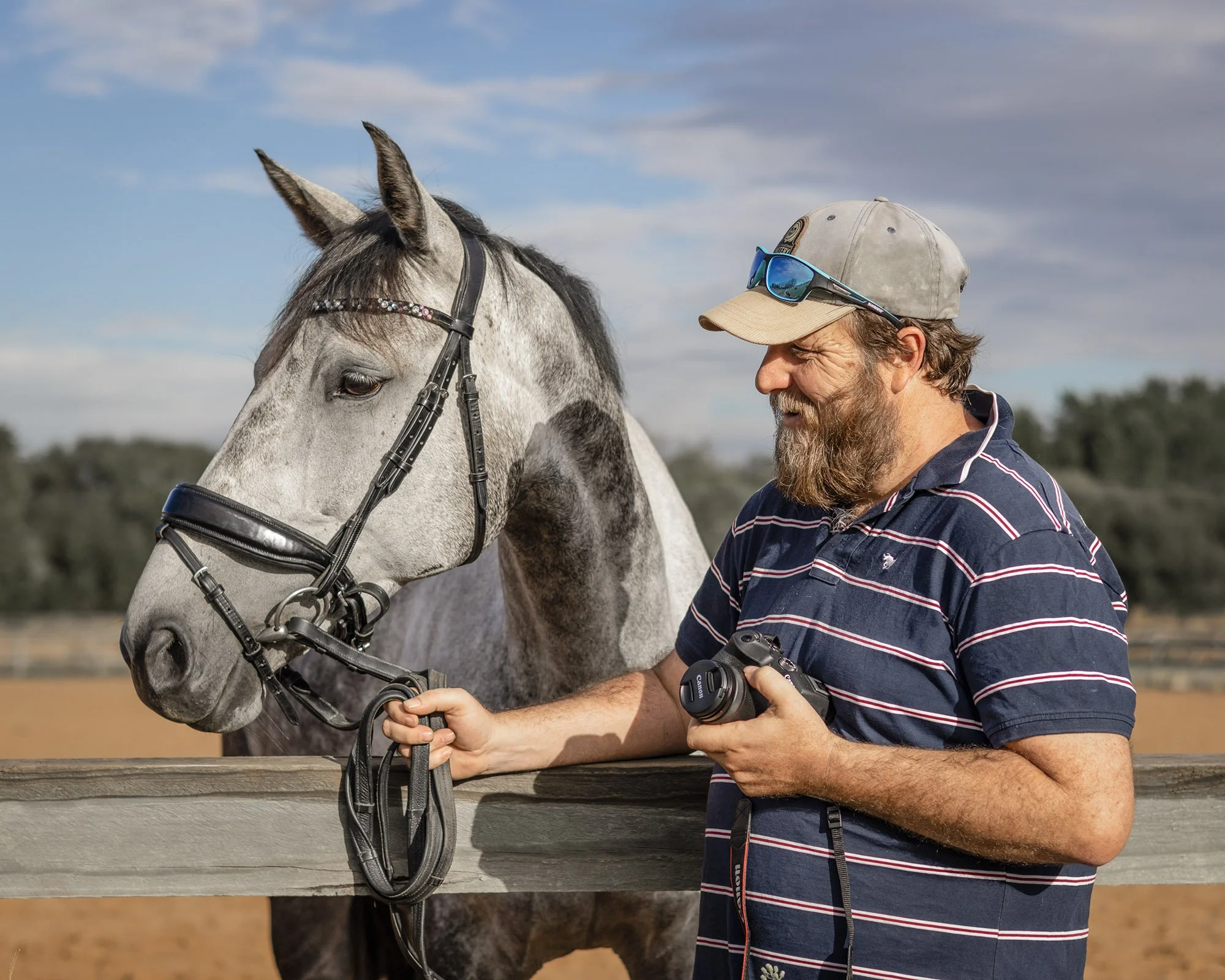 The image shows a man holding a camera in one hand and a beautiful dapple grey horse in the other