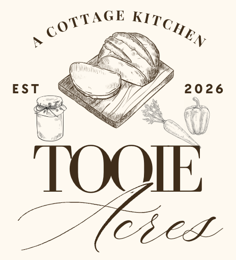 Graphic design featuring a loaf of bread on a cutting board, a jar of preserves, a carrot, and a bell pepper with the text 'A Cottage Kitchen EST 2026 Tooie Acres'.