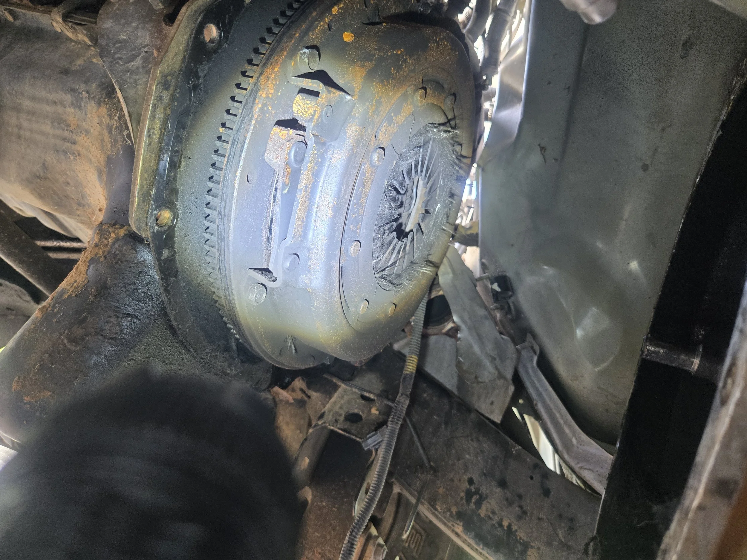 Close-up photo of a mechanical component inside a vehicle, showing rusty gears and metal parts with some wiring visible, indicating ongoing repair or maintenance work.