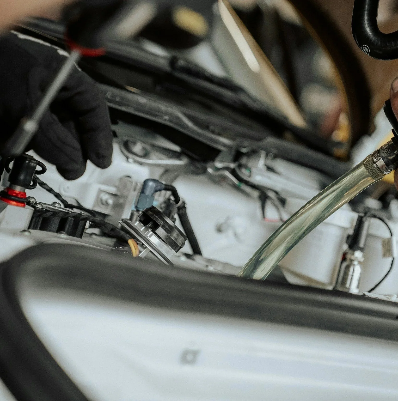 Close-up photo of a motorcycle engine with a person working on it, wearing a black glove, some tubes, wires, and mechanical parts.