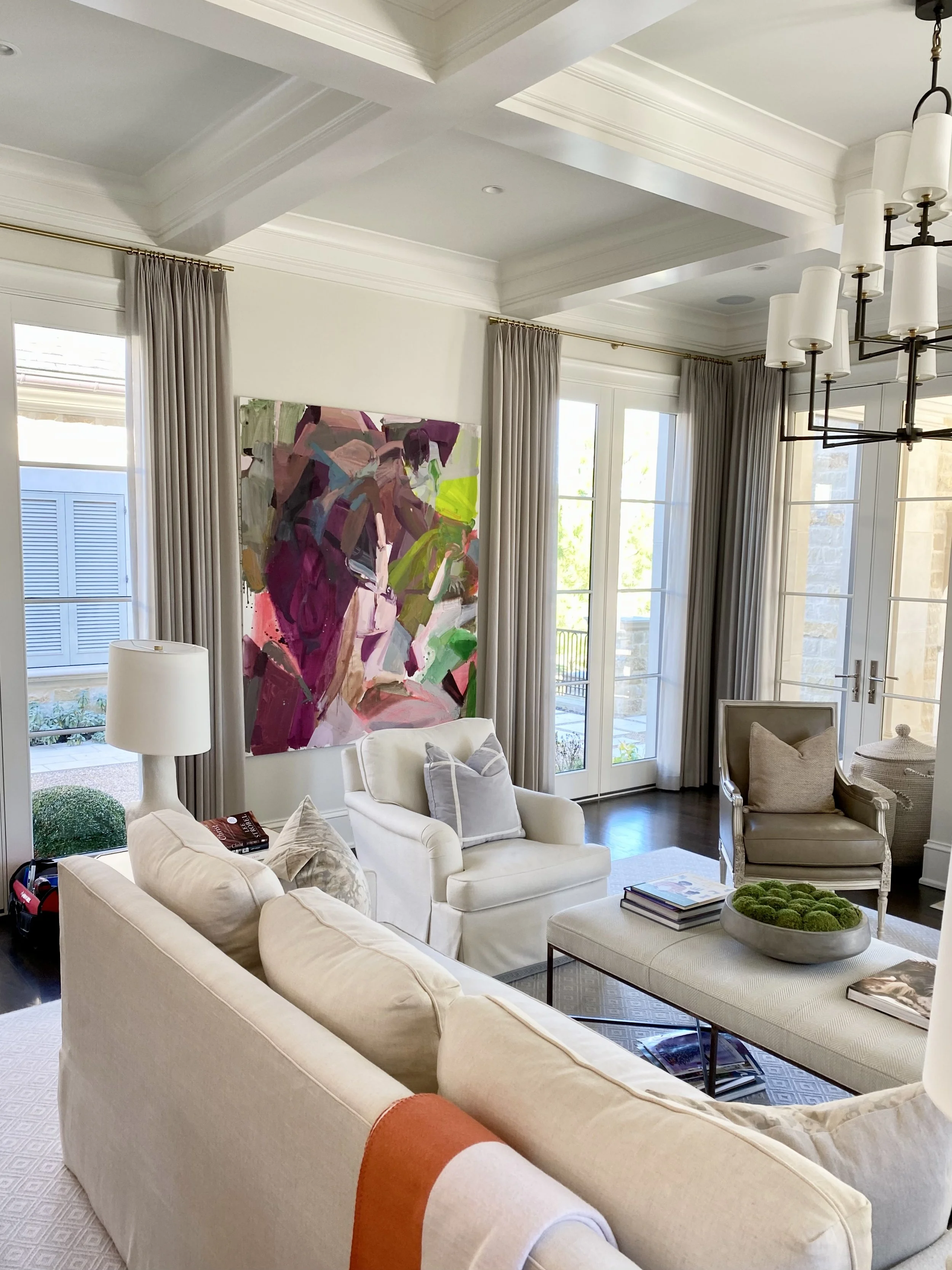 Comfortable contemporary traditional den with fireplace and coffered ceilings, bold paintings hang in the space.