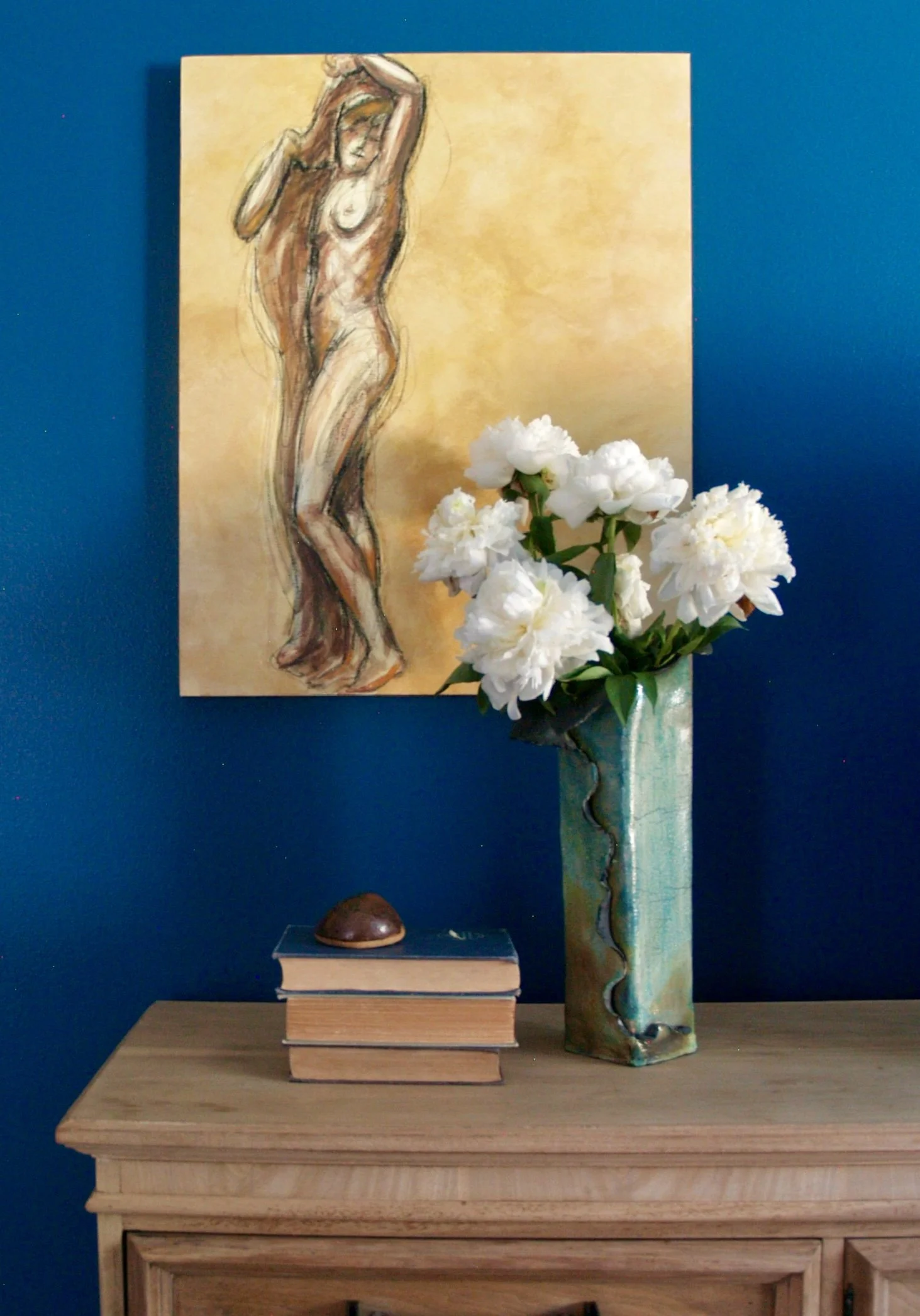 Saturated blue walls, stripped wood furniture, contemporary ceramics, nude drawing, flowers make up this primary bedroom.