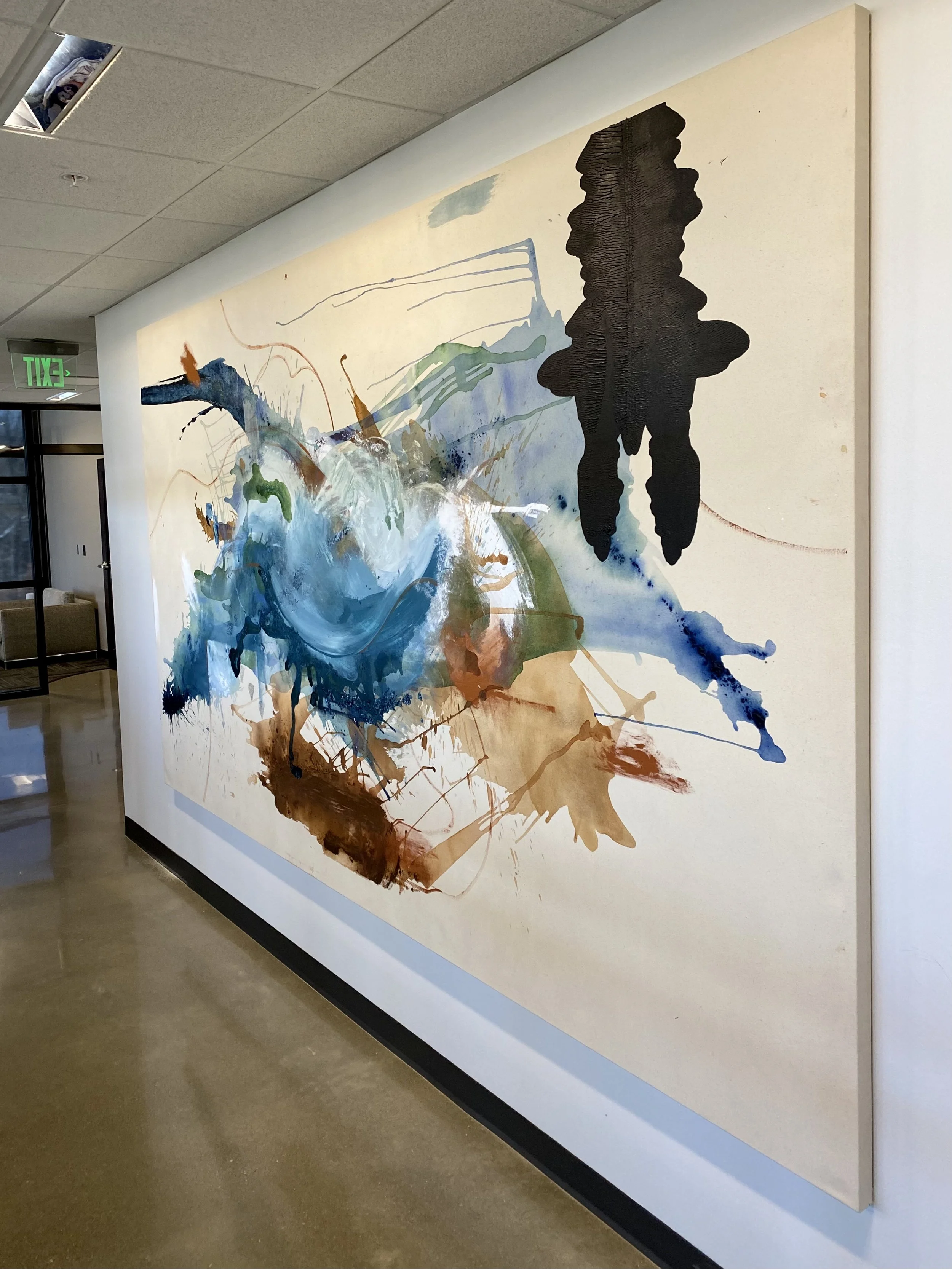 A large abstract watercolor painting on a gallery wall featuring splashes of blue, green, brown, and black ink, with a prominent black textured silhouette on the right side.