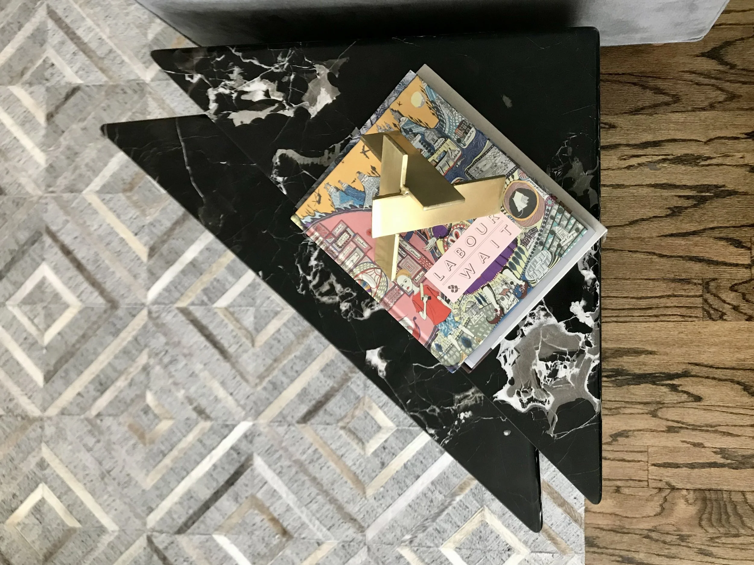 Gray, patterned hide rug, triangular black marble table, brass sculptural element with art books in this contemporary Austin home.