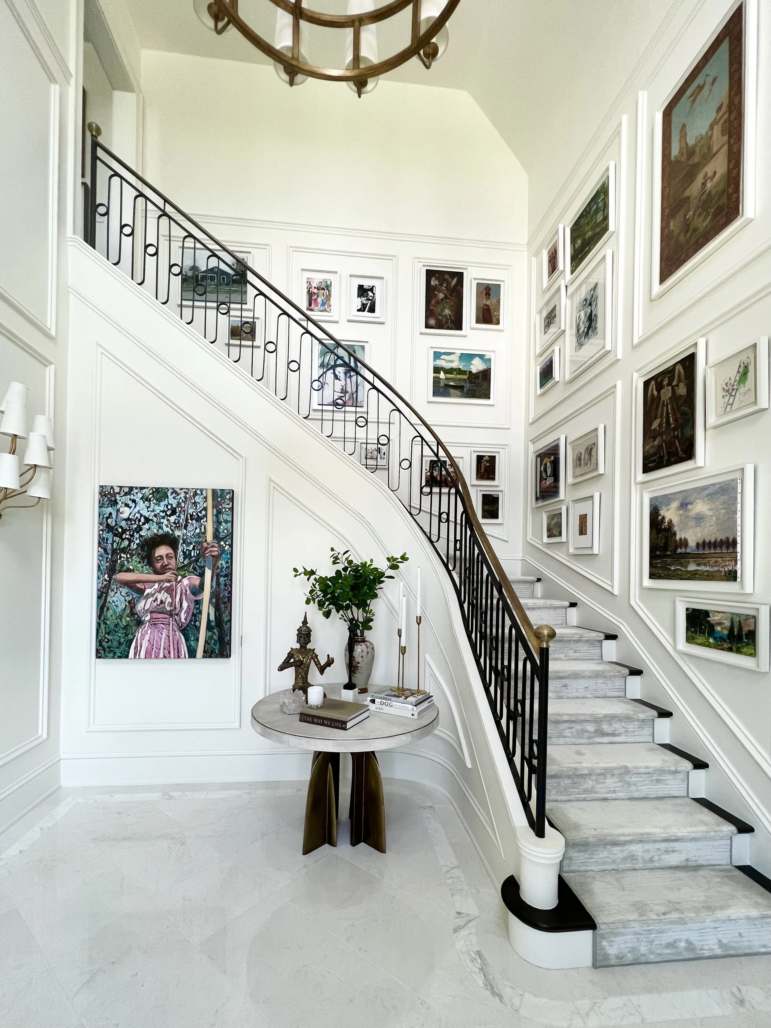 White walls and marble, contemporary metal stair rail, wood millwork create a grand stairwell, stacked from floor to ceiling in framed contarmporay and historic artwork. This luxurious new build melds contemporary and traditional elements for grand.