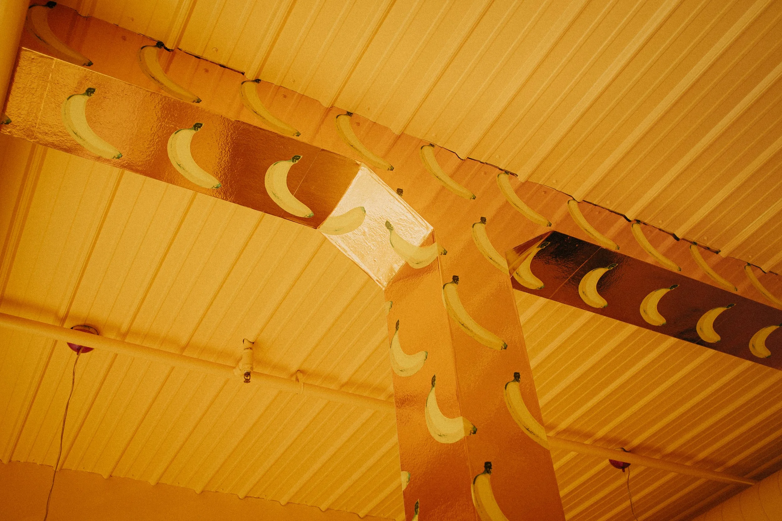 Decorative paper chains with banana illustrations hanging from a ceiling with wooden paneling.