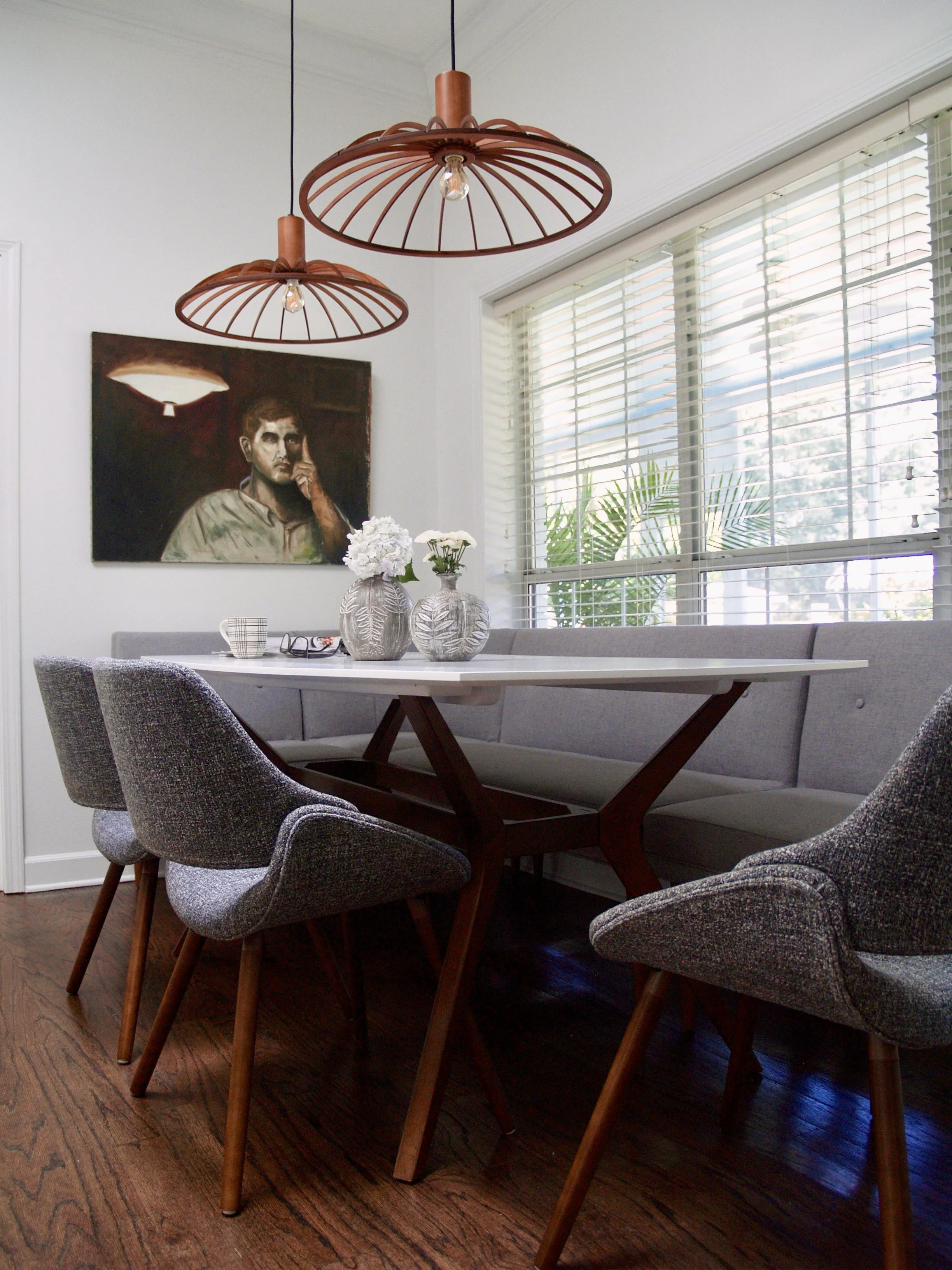 Dark wood floors, gray danish modern chairs and table, vintage portrait, and wooden architectural light fixtures define the breakfast nook of this contemporary traditional home.