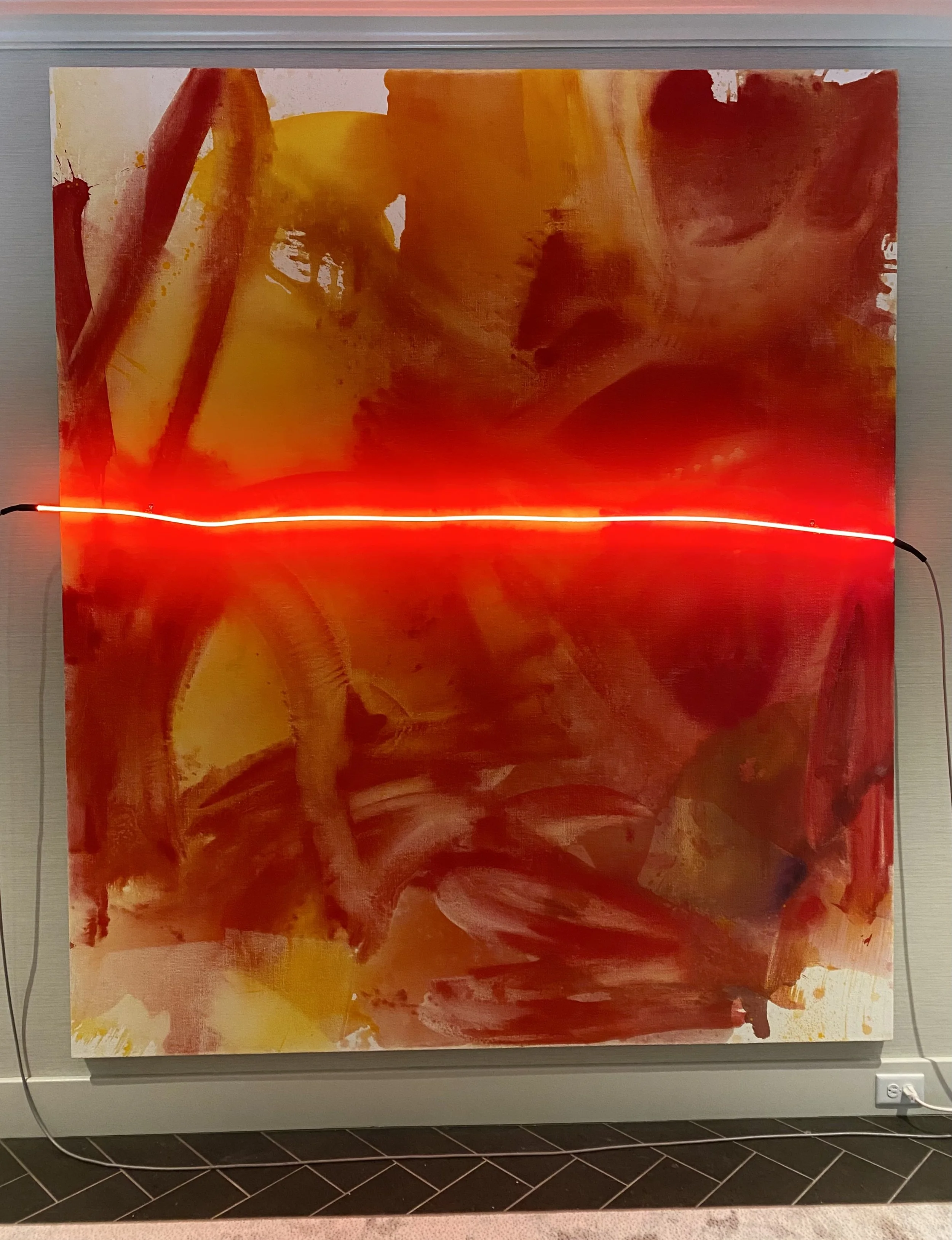 Abstract painting with warm colors including shades of red, orange, and yellow, displayed on a wall with a neon light strip along the bottom edge.