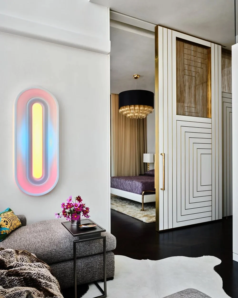 Modern living room and bedroom with geometric wall decor, colorful neon wall art, and a black and gold chandelier.