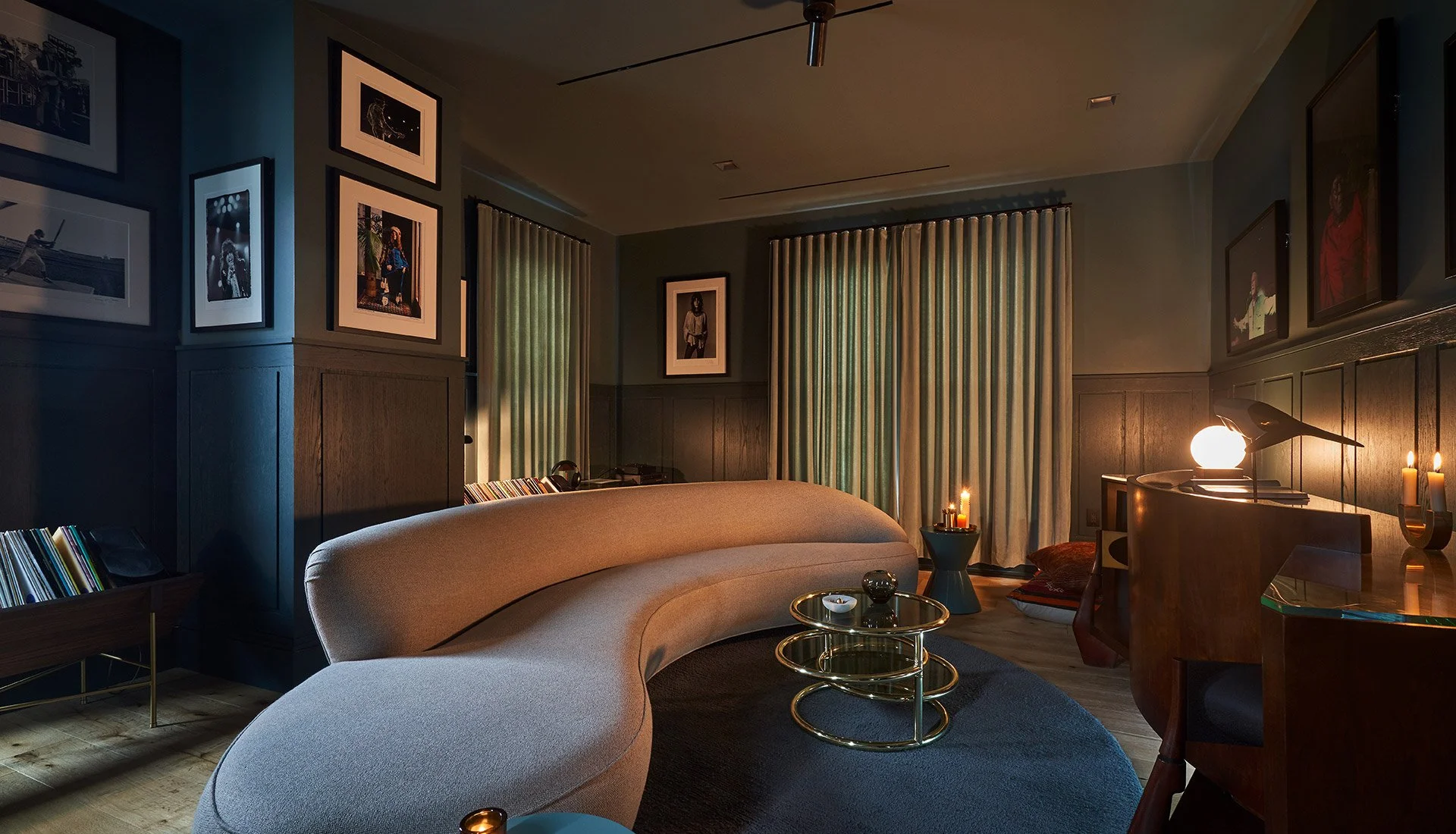 A sculptural contemporary curved sofa, in a dark saturated room, the walls stacked with framed photography of iconic musicians.