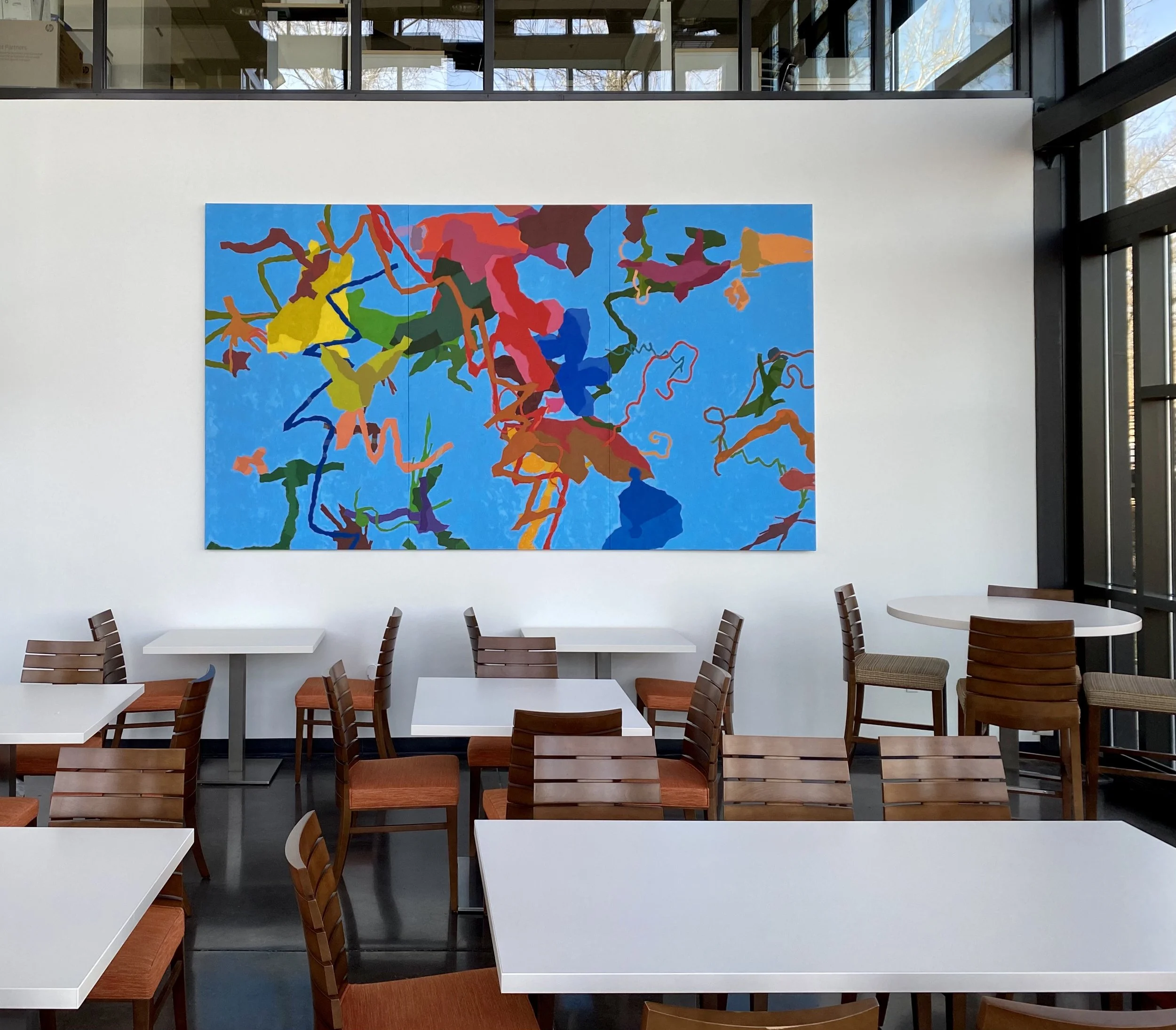 Interior of a dining area with white tables and wooden chairs, large colorful abstract artwork on the wall, and large windows letting in natural light.