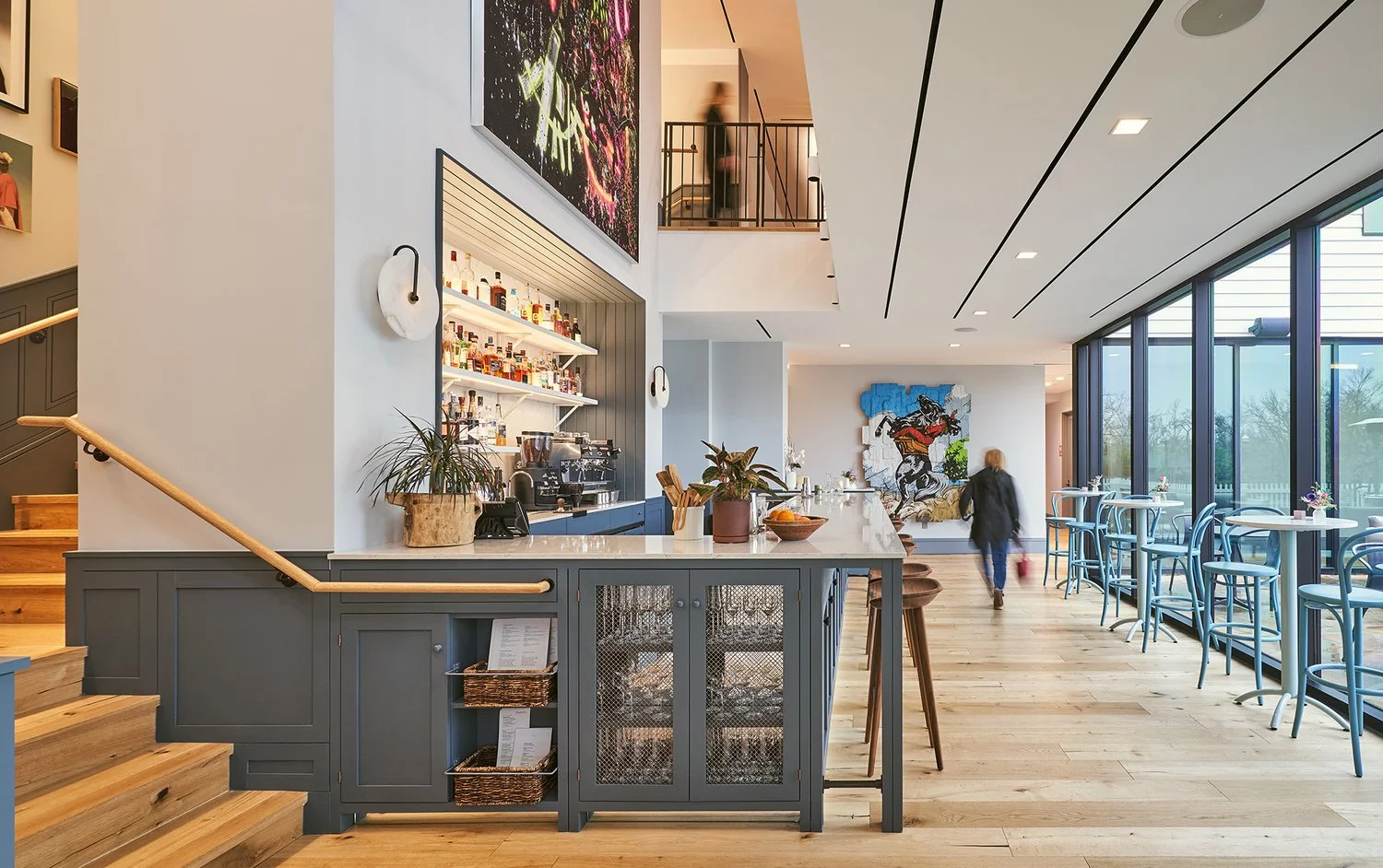 Contemporary, sophisticated double-height bar with wall of glass and contemporary artwork. Light wood floors, painted cabinetry, architectural space, and bold artwork define this contemporary restaurant space.