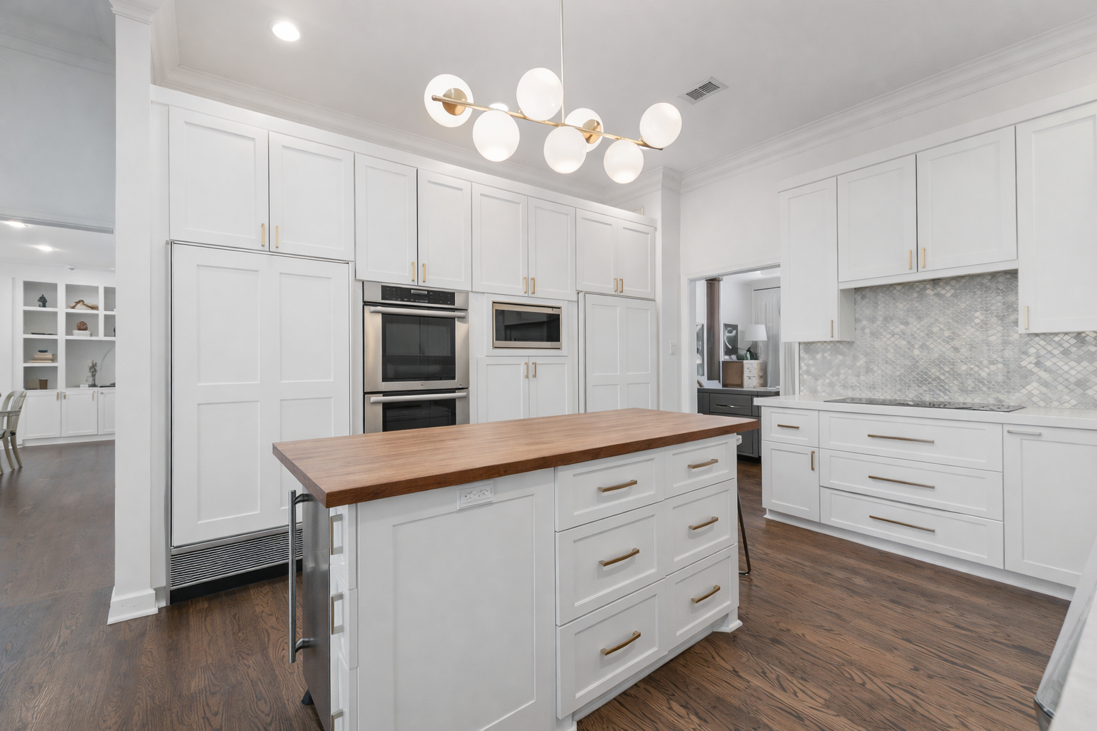 Dark wood floors, white cabinetry on this appliance wall, with butcher block topped island.