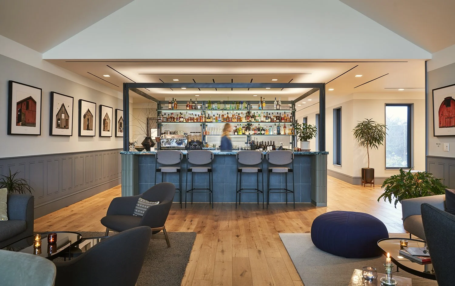 Architectural bar in lounge space of a hospitality room, barn artworks, plants, and sleek furniture line the comfortable, modern space.