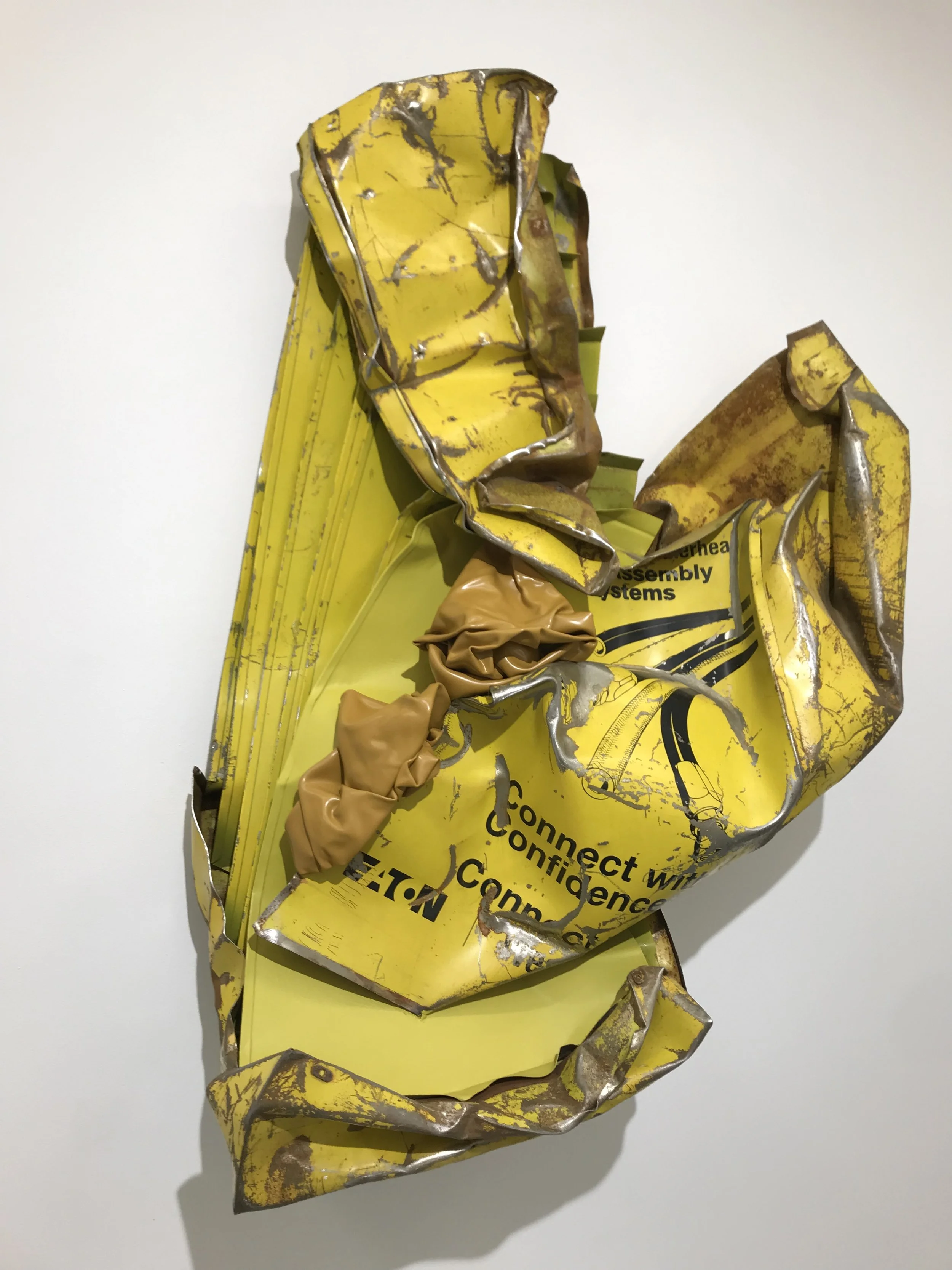 Crushed yellow promotional cardboard box with black text and metal wiring, lying on a white surface.