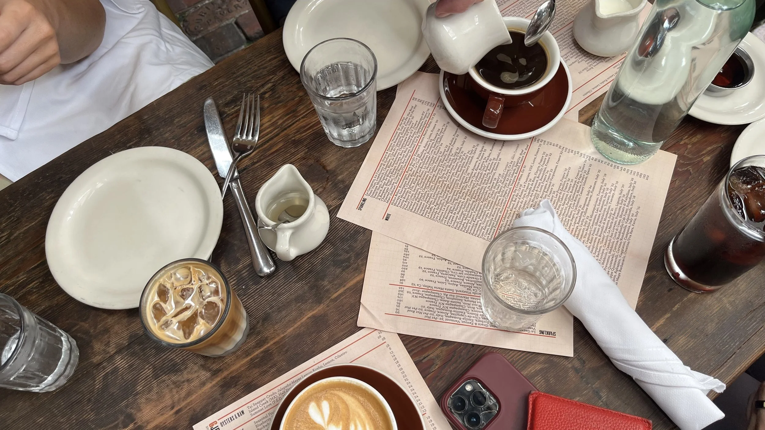 A table set with drinks including iced coffee and water, empty plates, cutlery, a menu, and condiments at a restaurant.