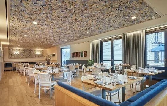 Wide plank white oak flooring, pink millwork, floral wallpaper on the ceiling throughout the space. Paintings and artwork along the side of the traditional yet contemporary dining room.