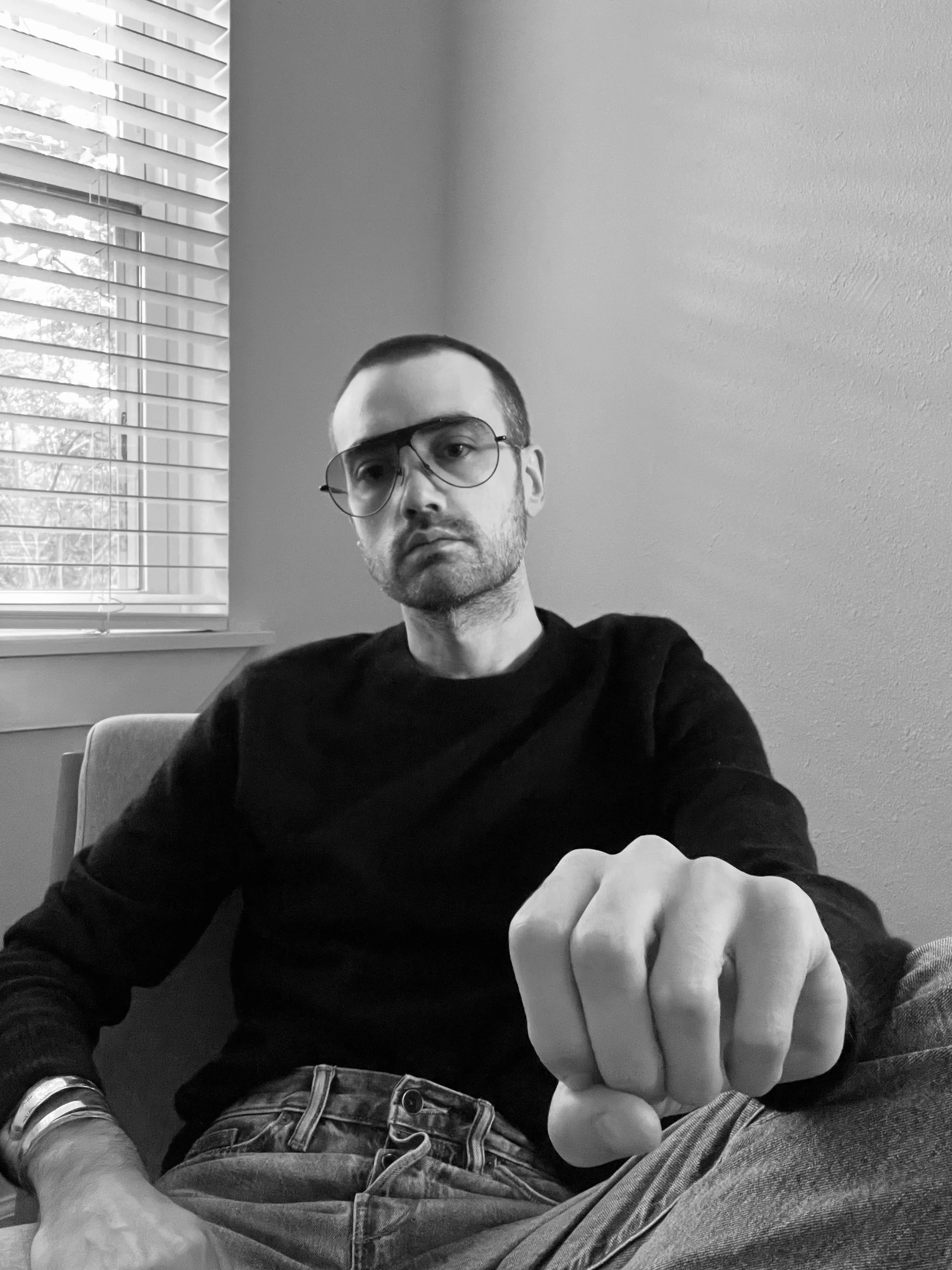 Black and White portrait of young man, shaved head, Jacques Marie Mage glasses. Designer and Art Advisor based in Austin, Texas with deep specialty in story and artistic pursuit. Former crystal bridges museum of American art curator.