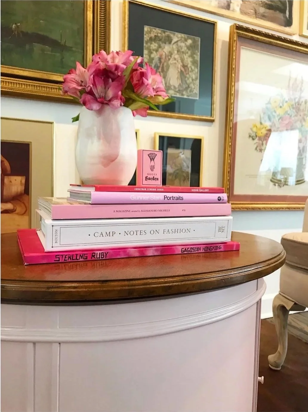 Historic pink table, contemporary ceramics, and pink stack of books color story n front of gallery wall.