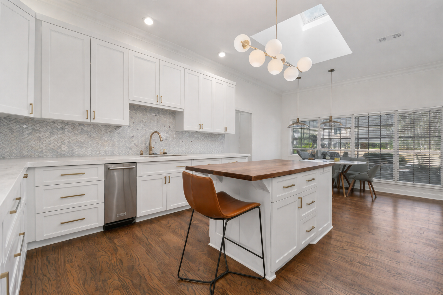 Light filled white kitchen, dark floors, skylight, white marble counter and backsplash, brash metal details make up this contemporary traditional kitchen in Austin Texas.