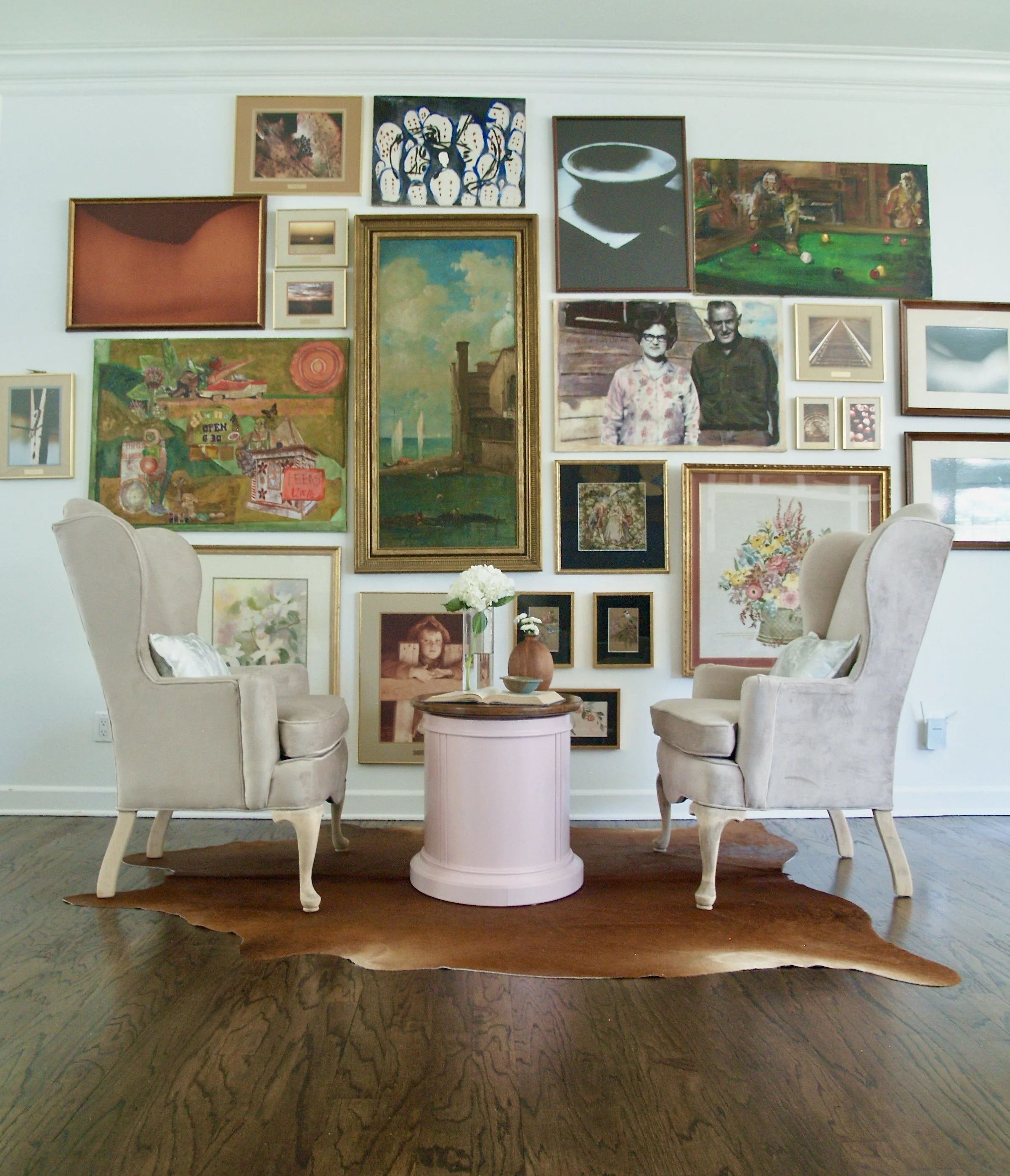 Eclectic gallery wall of contemporary and historic works behind pink velvet wingback chairs on a cowhide rug. This contemporary traditional home is designed by Dylan Turk of Austin Texas.