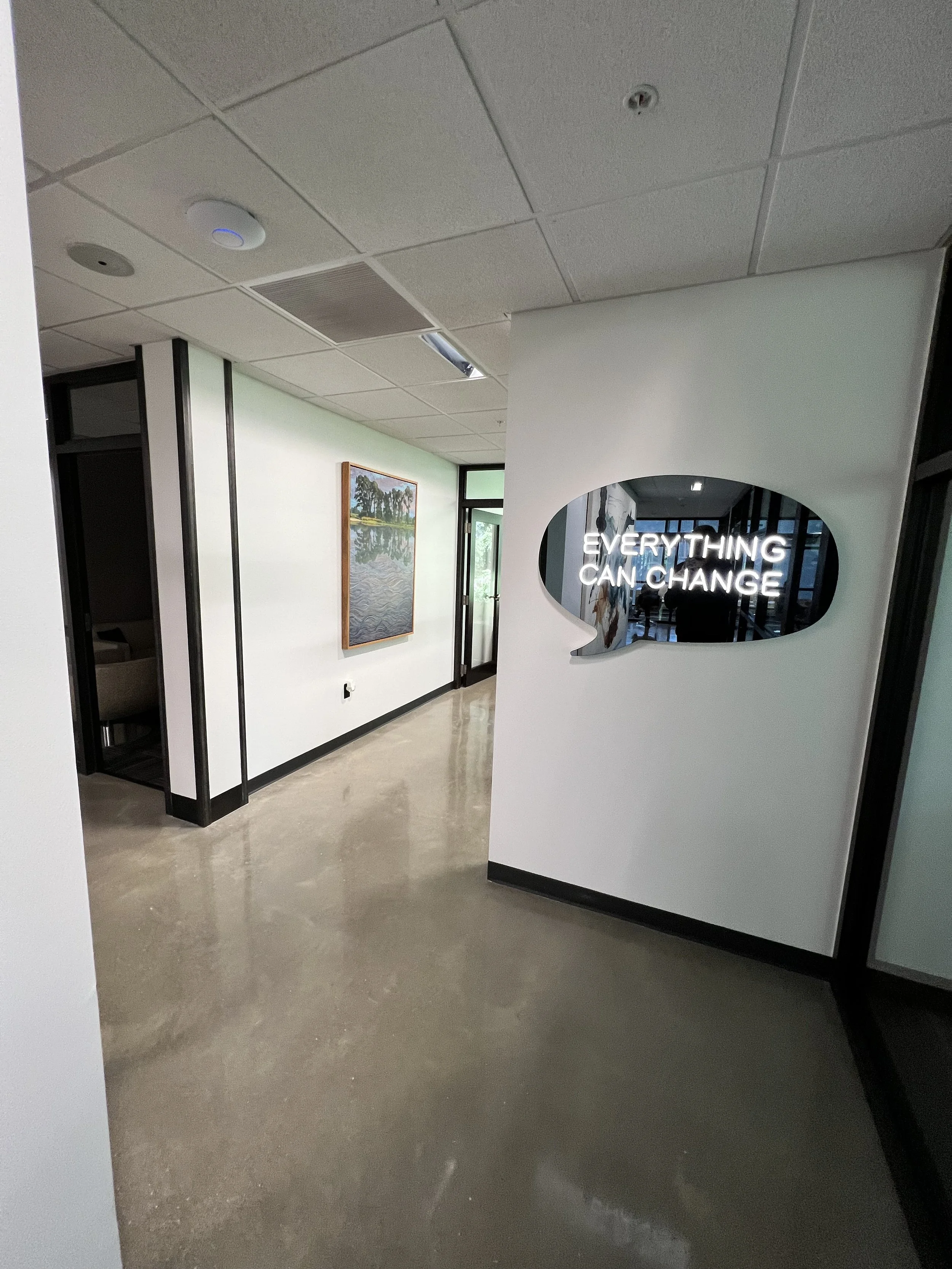 Photo of an indoor space with a white wall display reading 'EVERYTHING CAN CHANGE' with a photograph of trees and water in the background, and a painting on the wall.