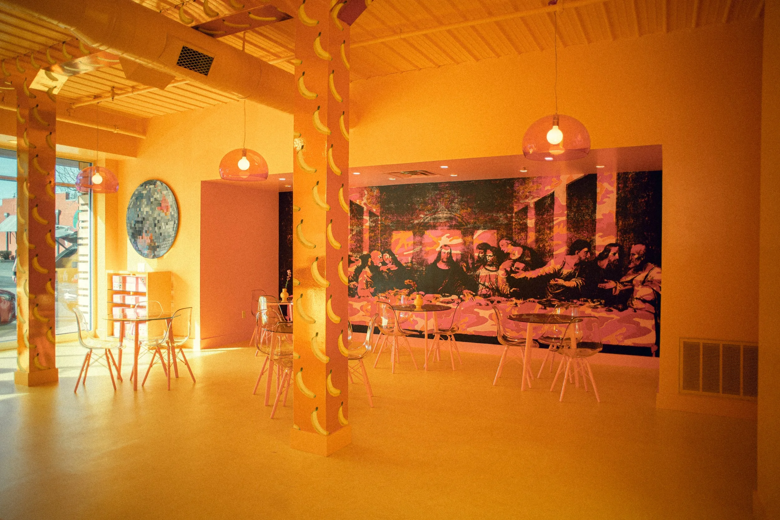 Bold, marigold saturated room punctuated with Flavor Paper wallpaper, Andy Warhol After The Last Super mural, and acrylic Eames ghost chairs designed by Dylan Turk. A bright commercial, restaurant, and retails space with an artistic point of view.