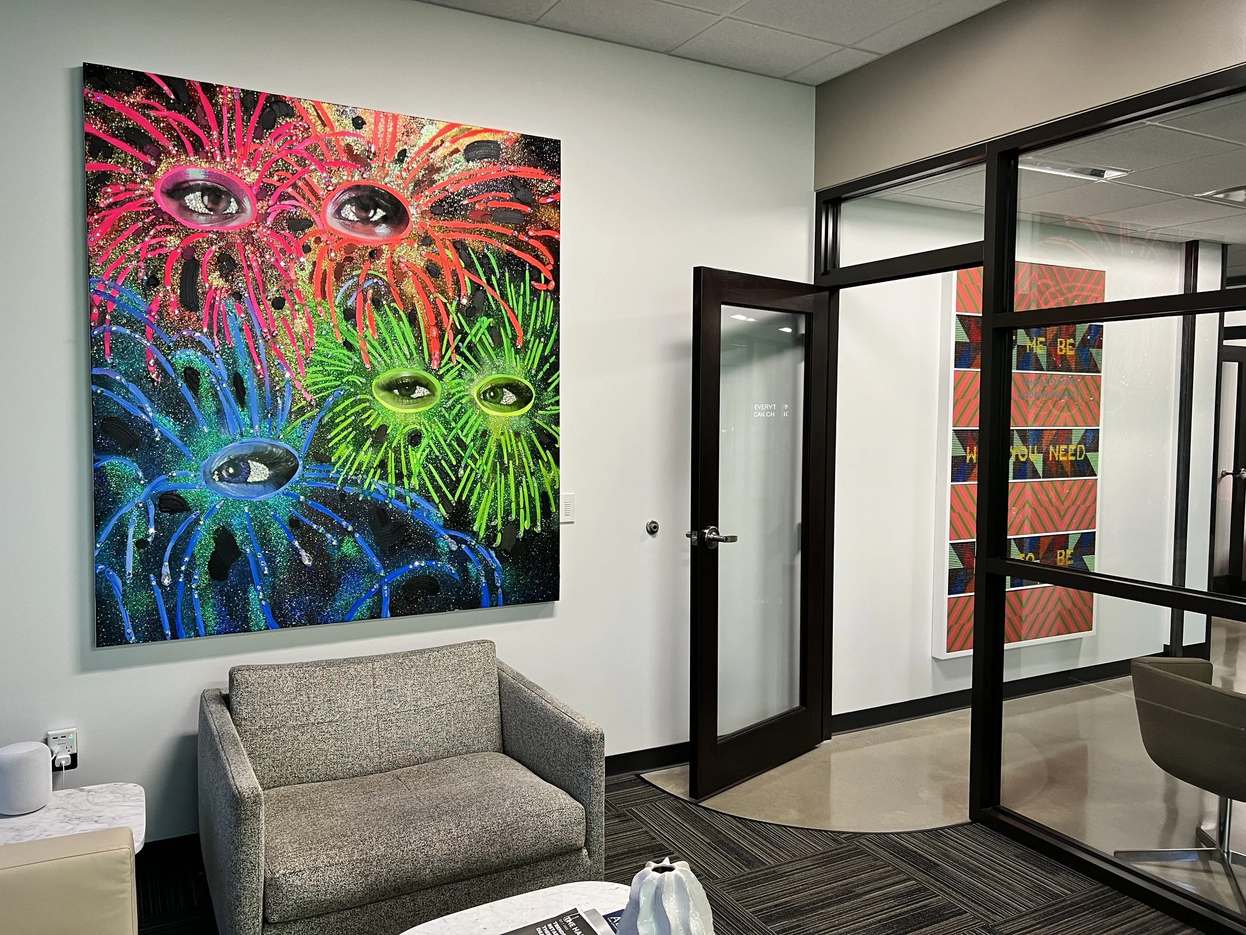 An office waiting area with a colorful abstract painting on the wall, gray sofa, marble side table, and office glass door.