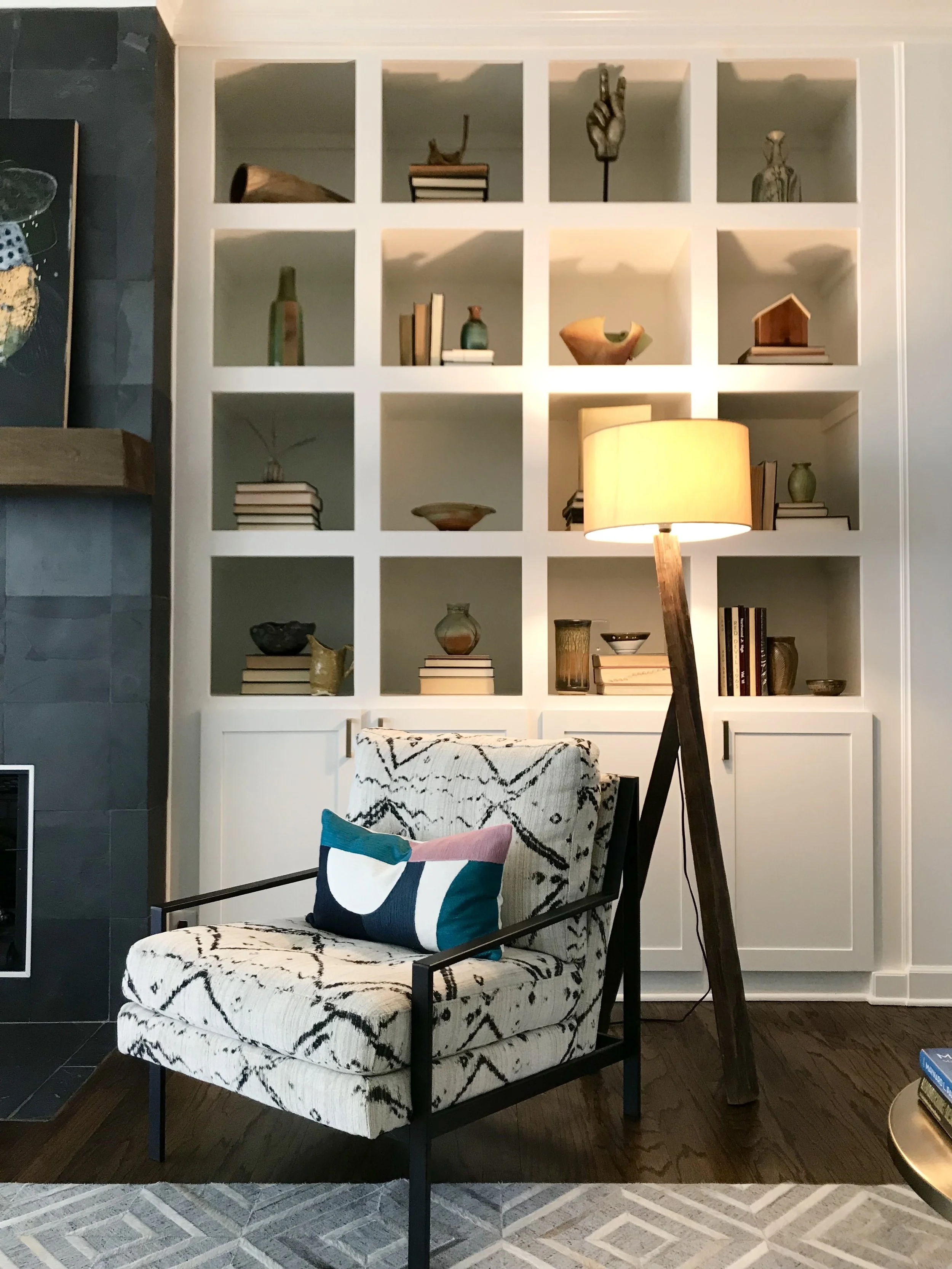 Hide rug, colorful metal and upholstered chair, and a builtin cabinet displaying a ceramic collection.