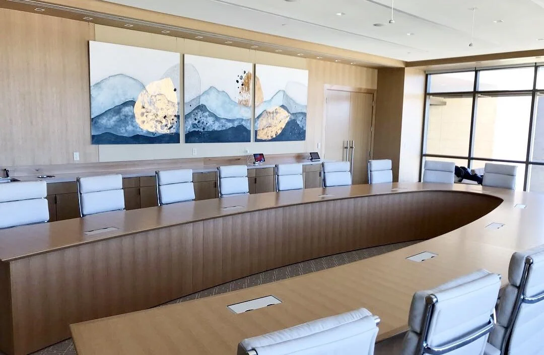 Empty conference room with a large wood table, white chairs, large window, and mountain-themed artwork on the wall.