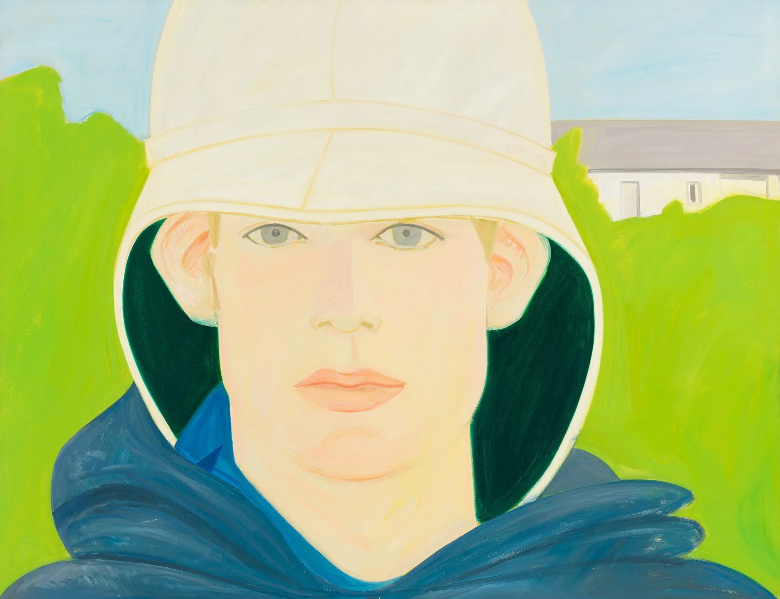 A portrait of a person wearing a light-colored hat and a dark blue hoodie, with a background of green foliage and a building in the distance.
