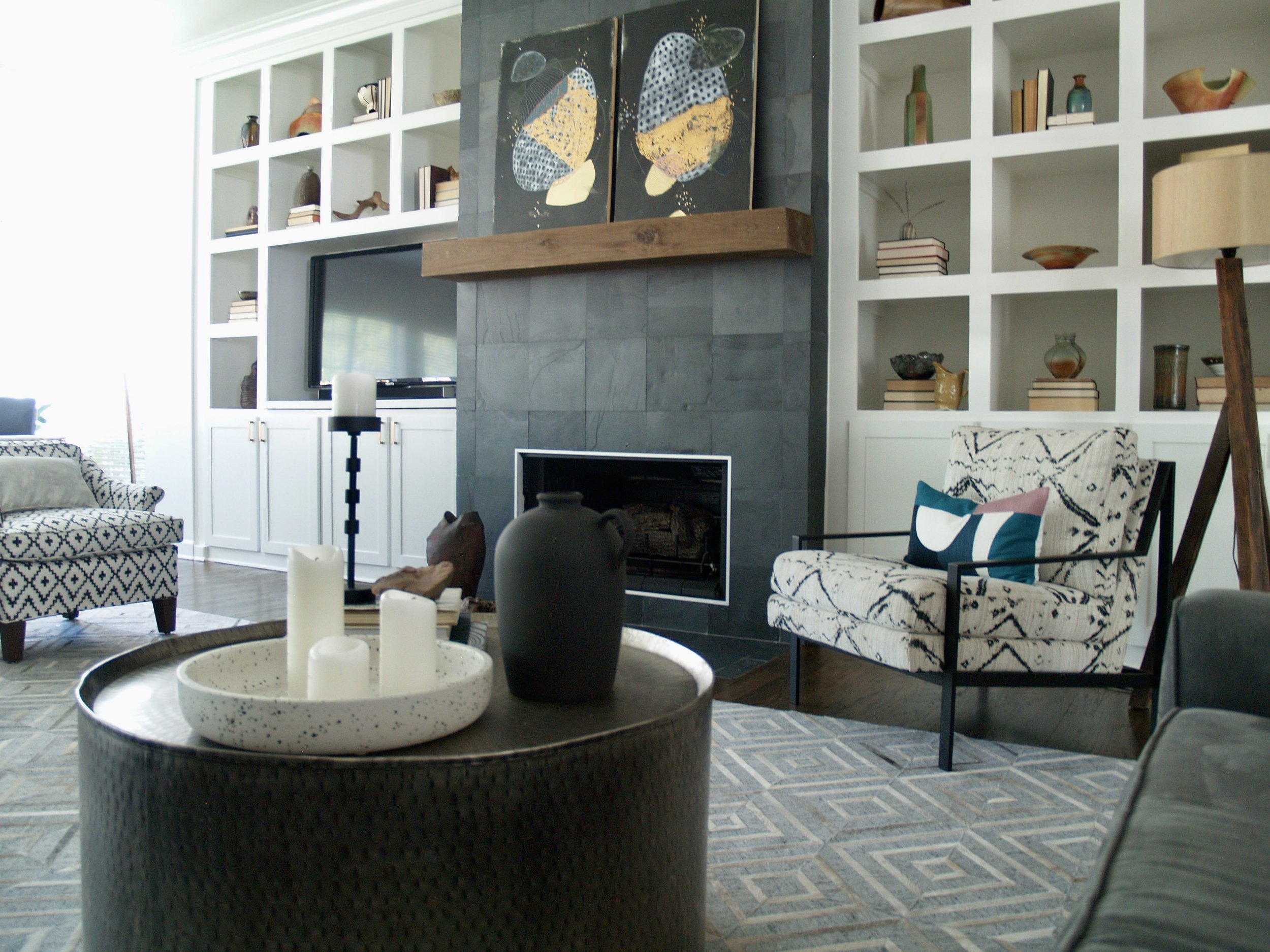 Slate contemporary fireplace, with builtin shelving displaying ceramics collection. Bold, eclectic living room comprised of hide rugs, metal tables, wood beams, and a pattern play bound by color. Designed by Austin based designer Dylan Turk.