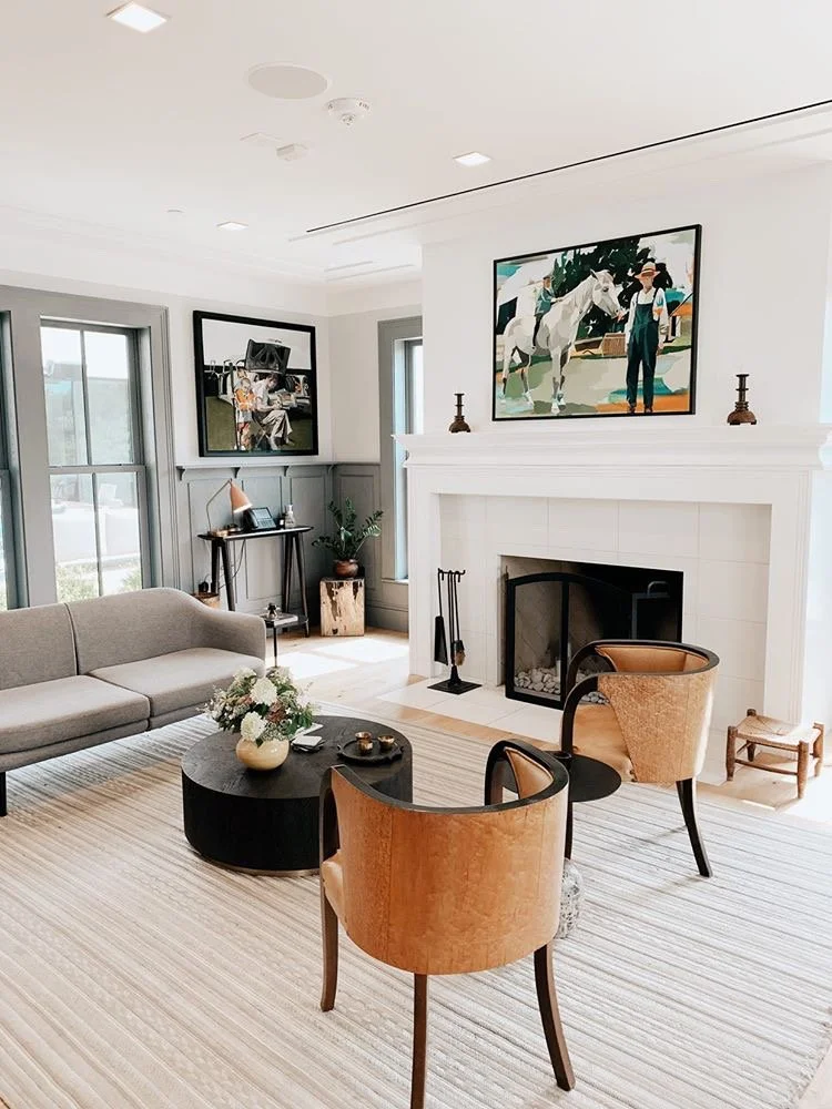 A tight seating of calm furniture, surround a traditional fireplace with paintings of a man and a horse colorful above it.