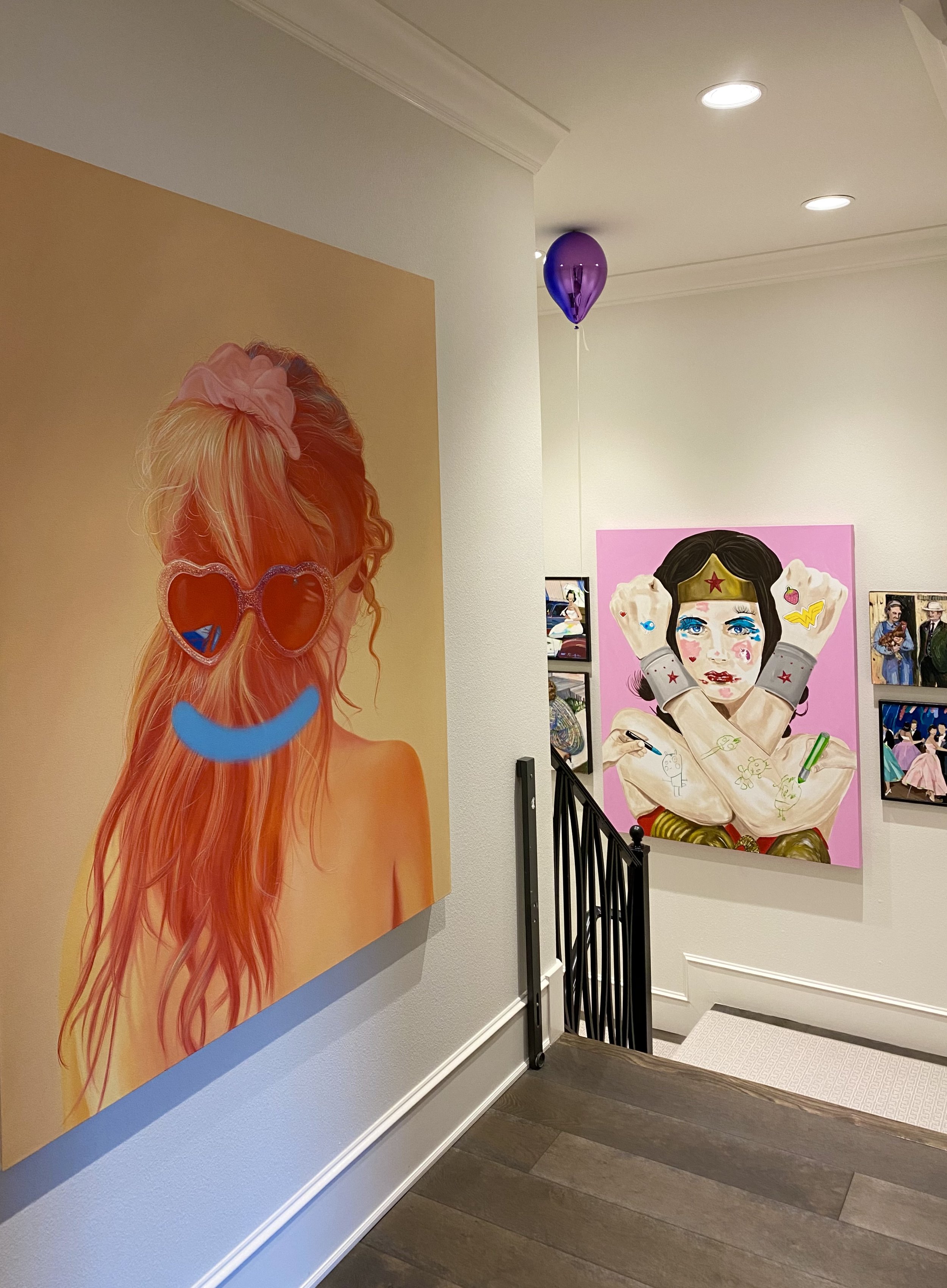 Art gallery interior with colorful posters, including a portrait of Wonder Woman with fists raised, and a purple balloon floating near the ceiling.