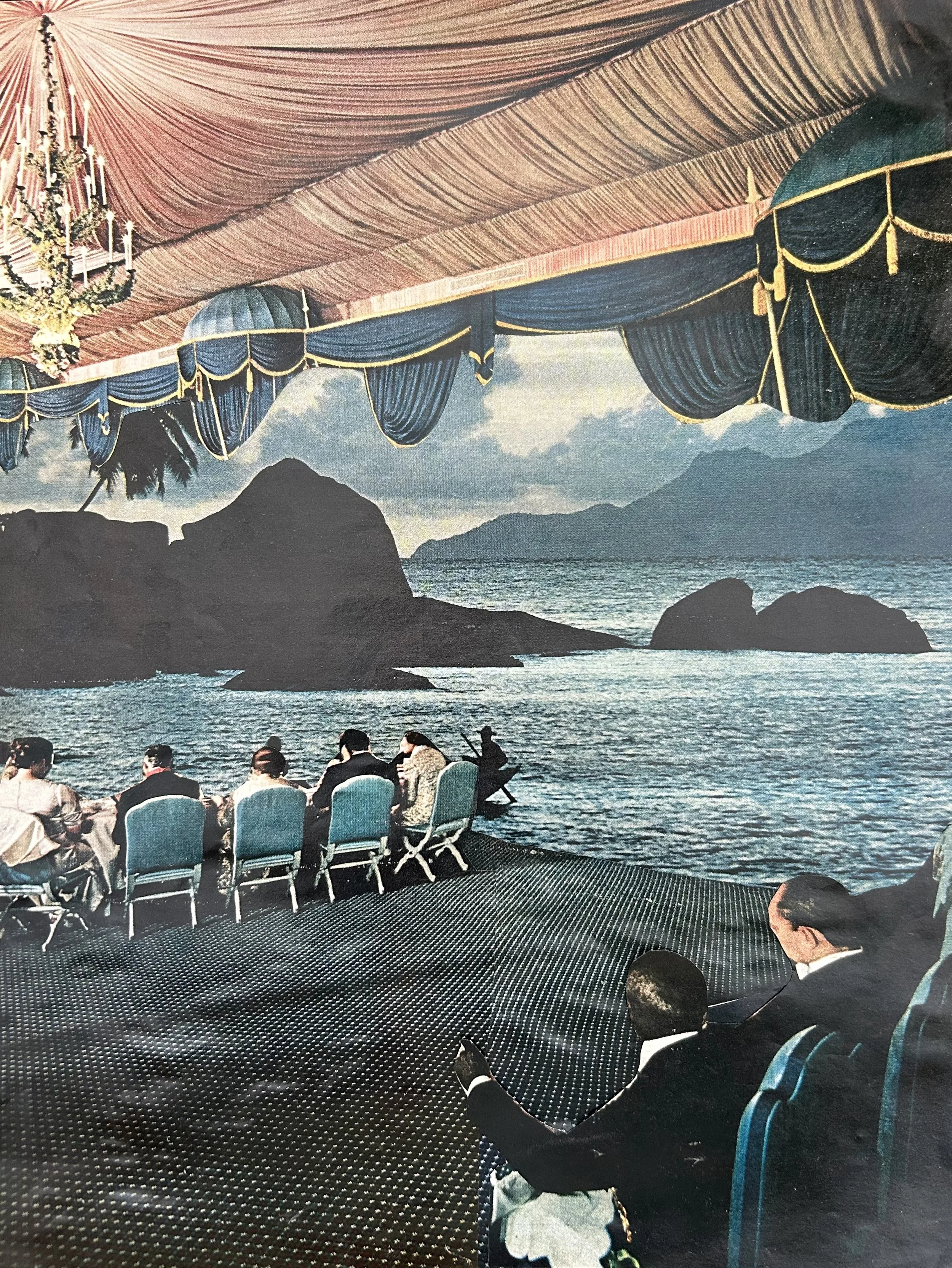 People sitting on chairs on an indoor stage with an ocean view and mountains in the background, decorated with a chandelier and drapes.